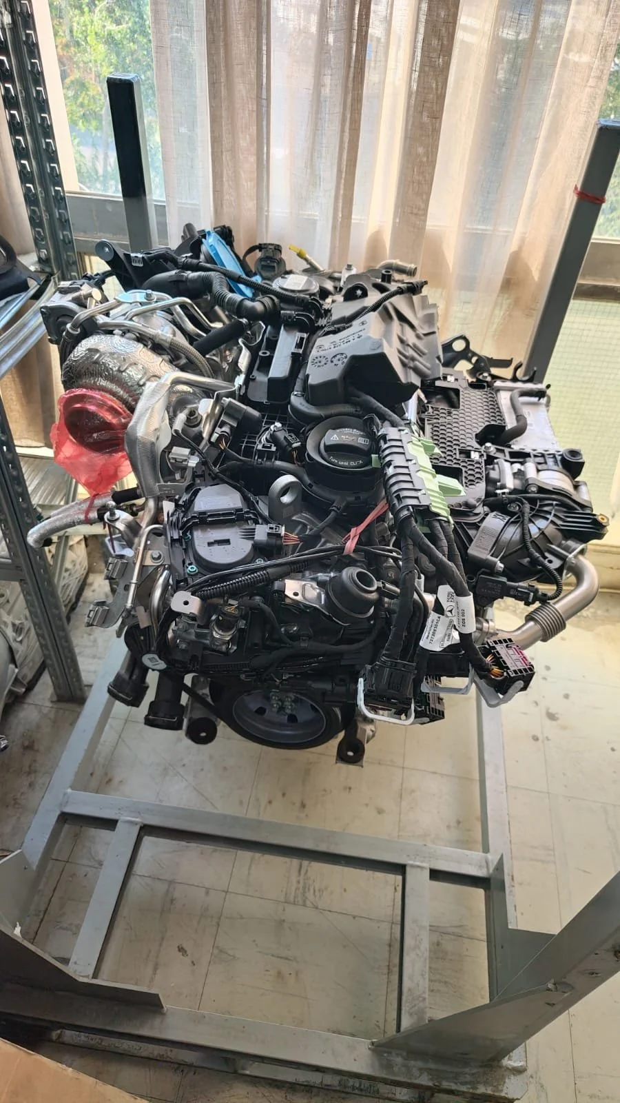 Automobile engine on a metal stand in a workshop, with tools and equipment in the background.