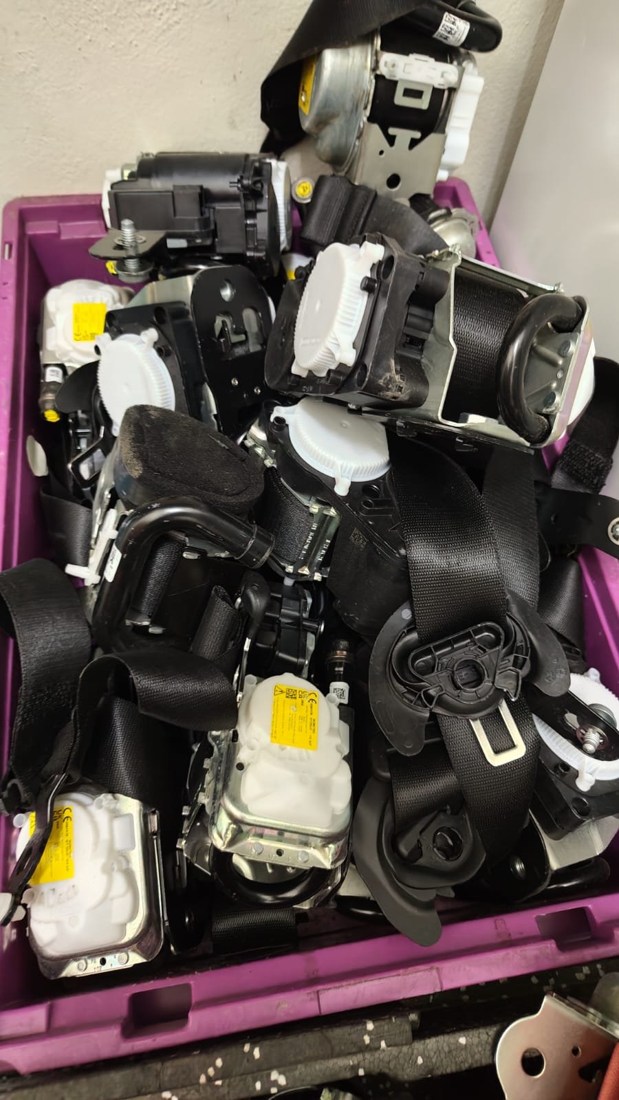 A pink plastic bin filled with various disassembled electronic or mechanical parts, including black straps, white plastic containers, and metallic components.