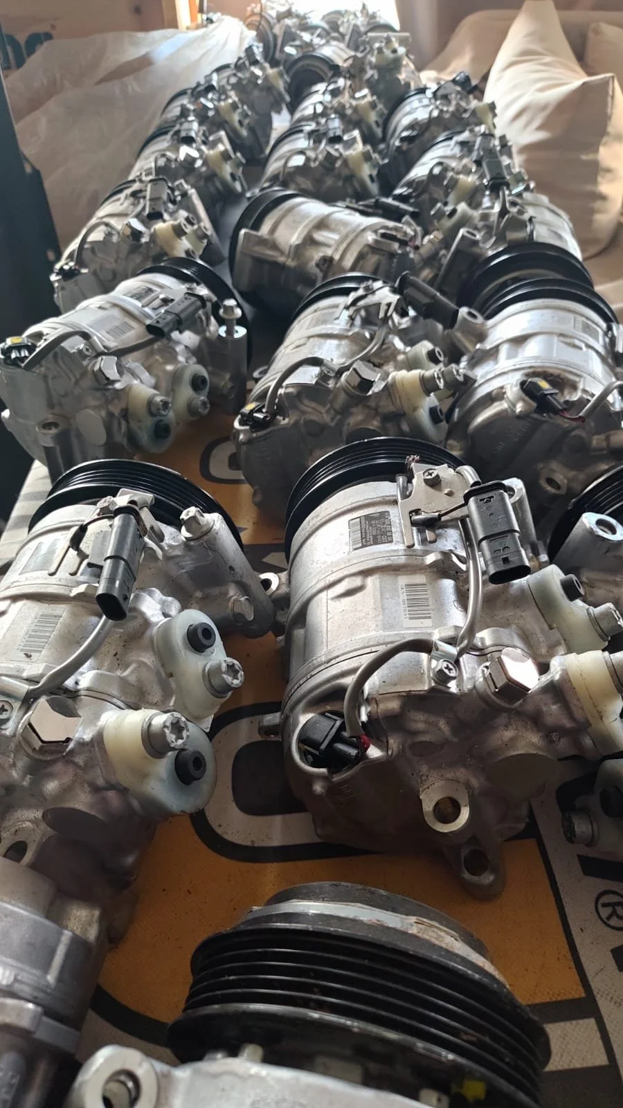 Multiple automotive air conditioning compressors and pulleys laid out on a surface.