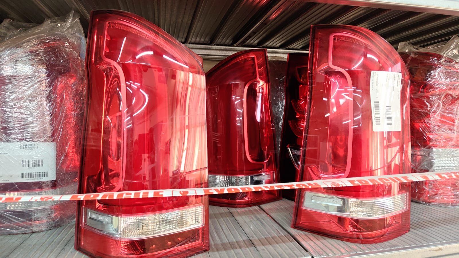 A stack of red and clear car tail lights on a wooden shelf, surrounded by warning tape labeled 'EXPLOSIVE'.