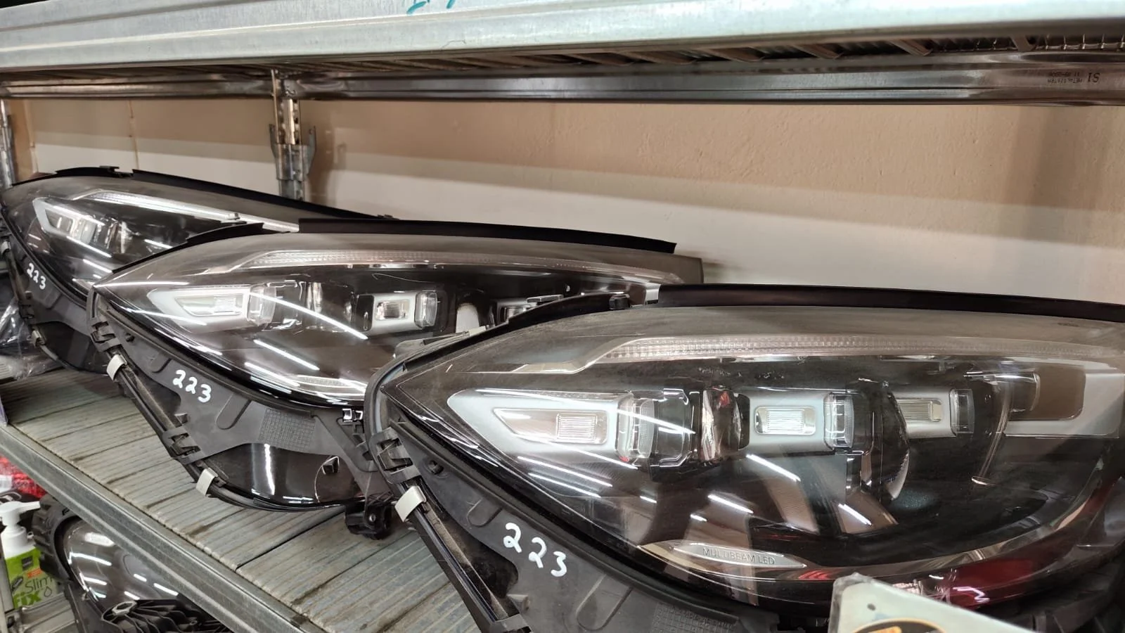 Multiple black car headlights arranged on a shelf in a store, with one in the foreground showing LED lights and a label reading '223'.