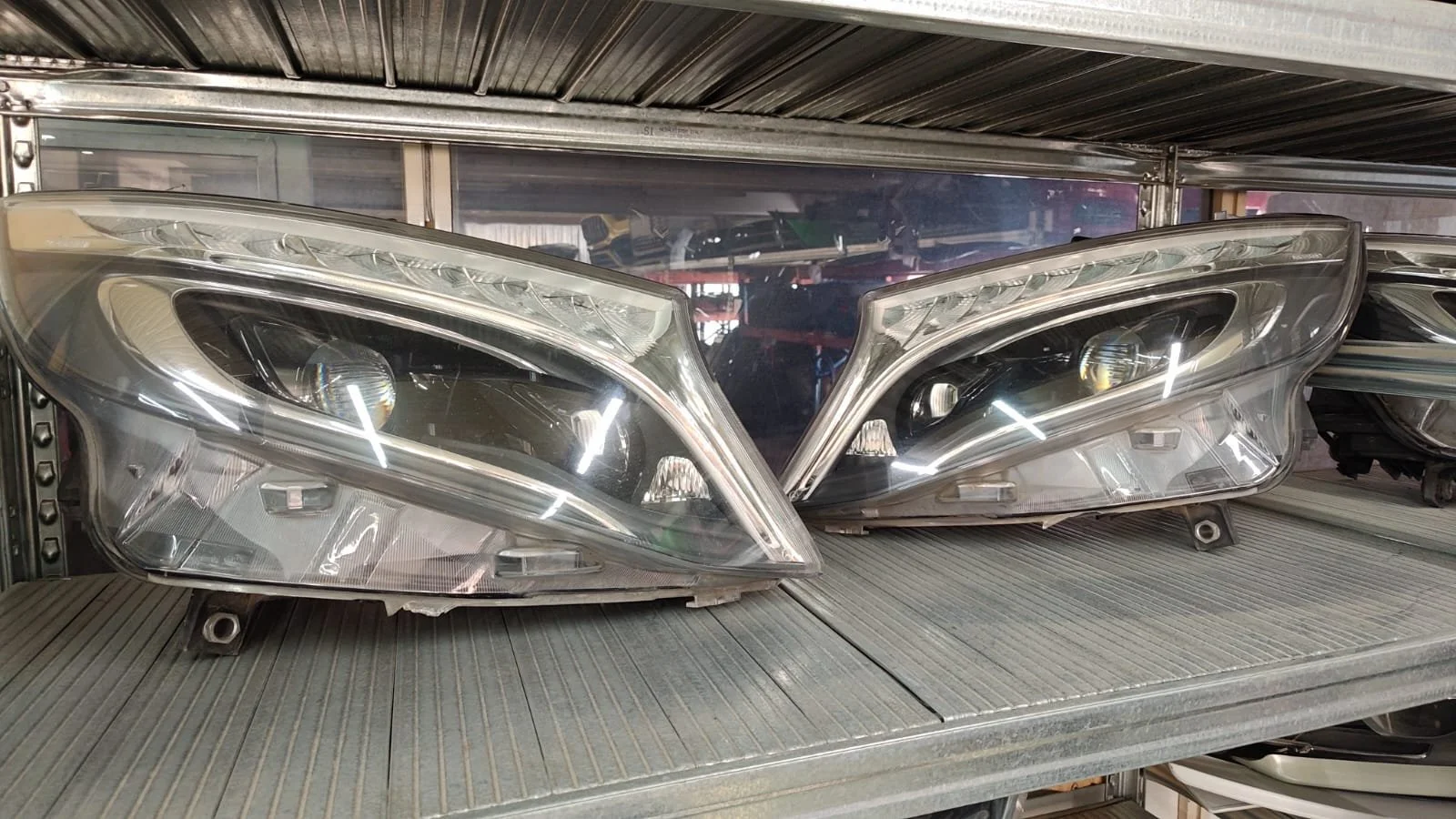 Pair of car headlights on a metal shelf in a store or workshop.