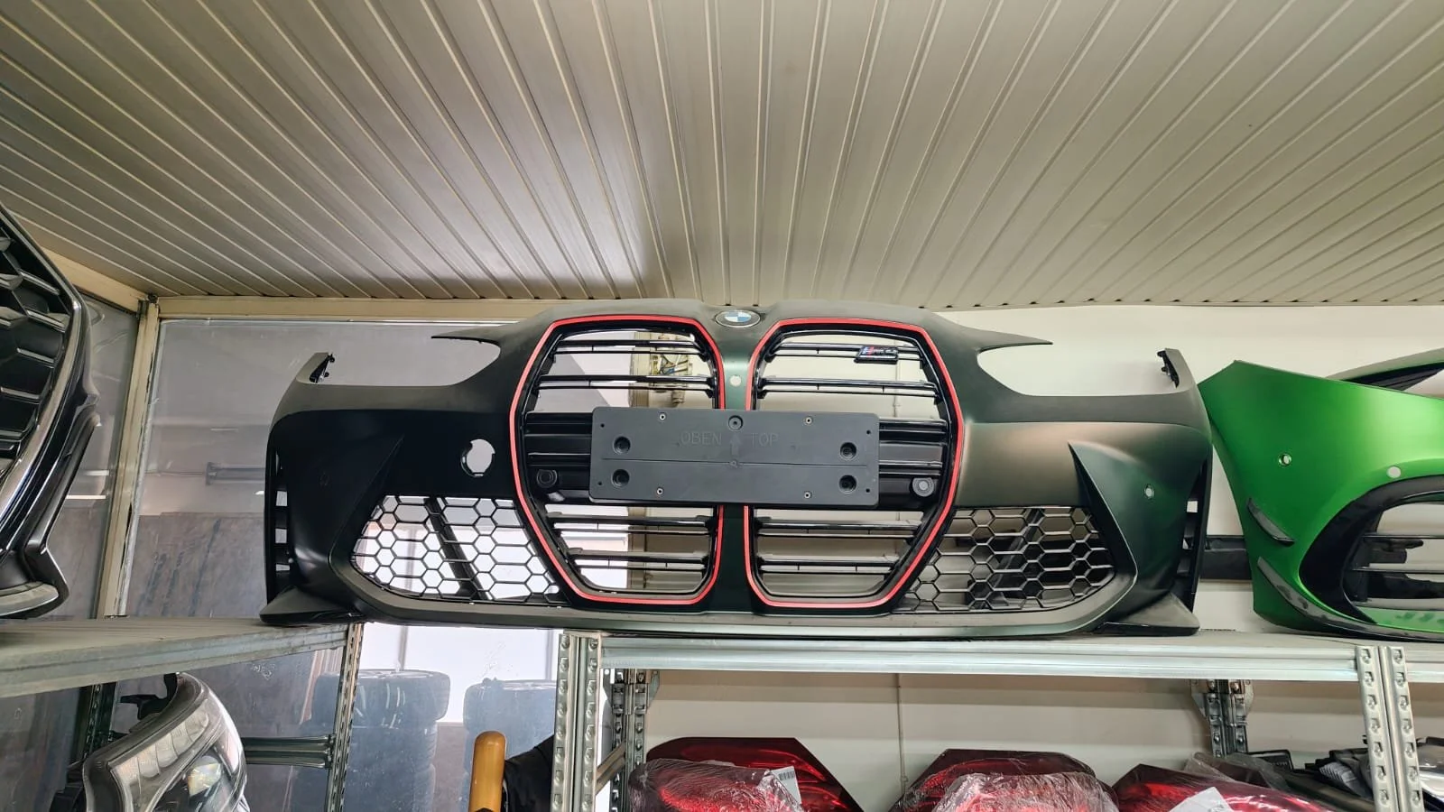 Car front grille with black honeycomb pattern and red outline, mounted on a shelf in a workshop.