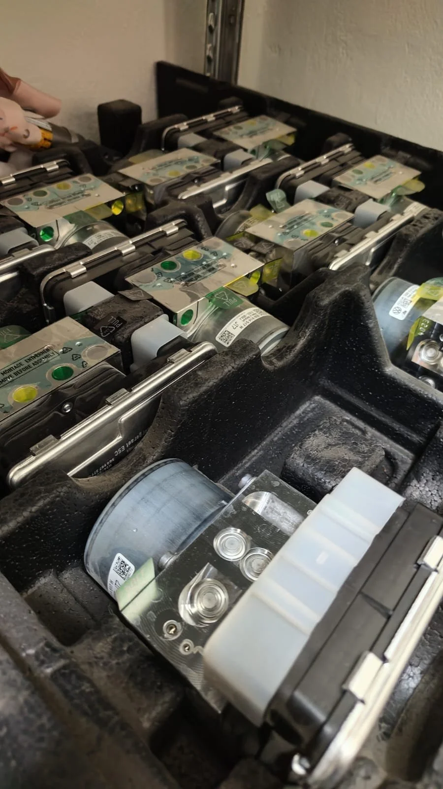Close-up view of a mechanical or electronic device with multiple cylindrical components, metal parts, and labels, possibly an industrial machine or parts of a vehicle.
