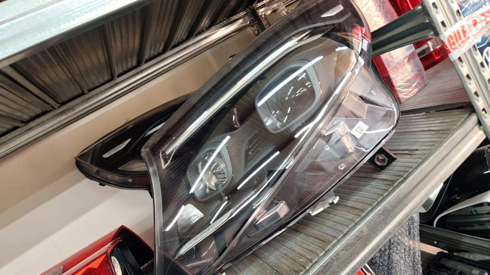 Car headlight on a shelving unit with other car parts around.