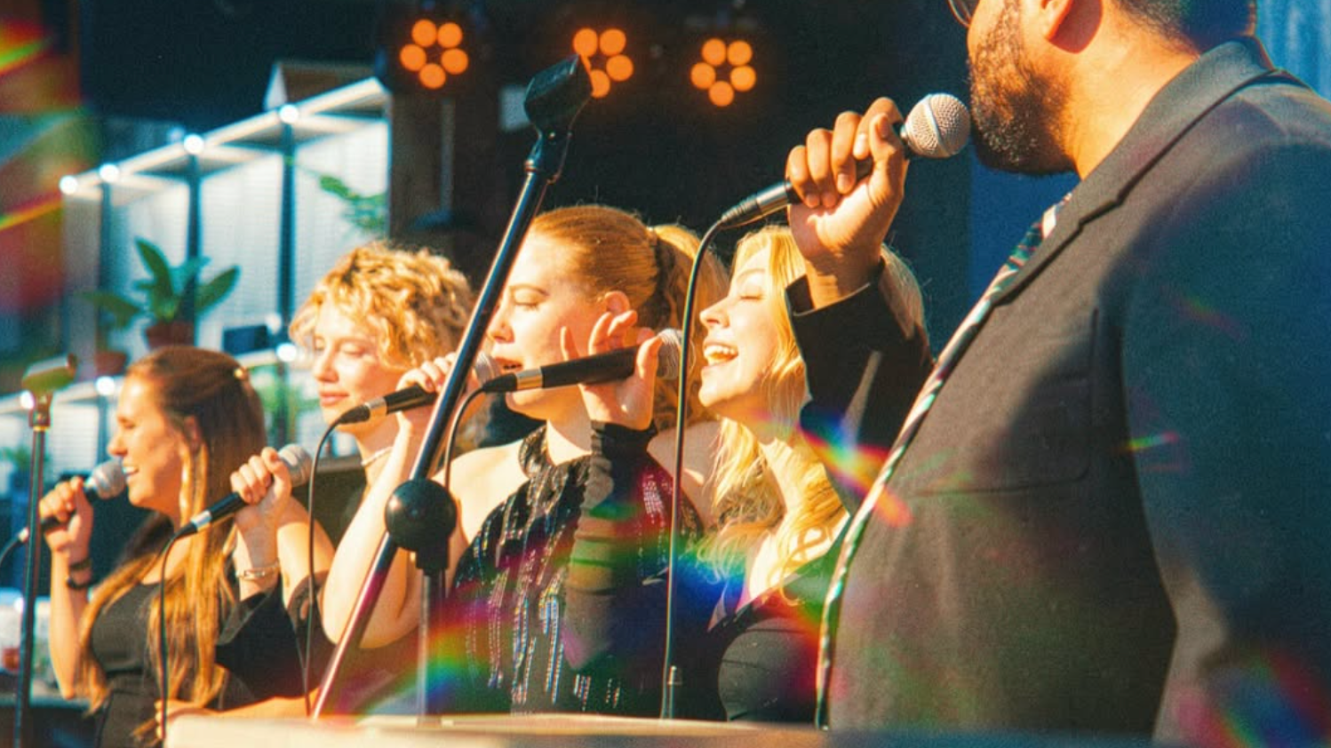 People singing into microphones on stage with colorful lighting
