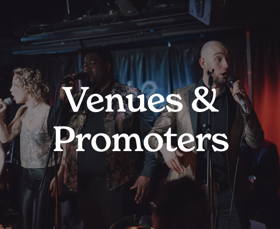 A group of performers on stage singing into microphones, with a backdrop that reads 'Venues & Promoters' in white text.