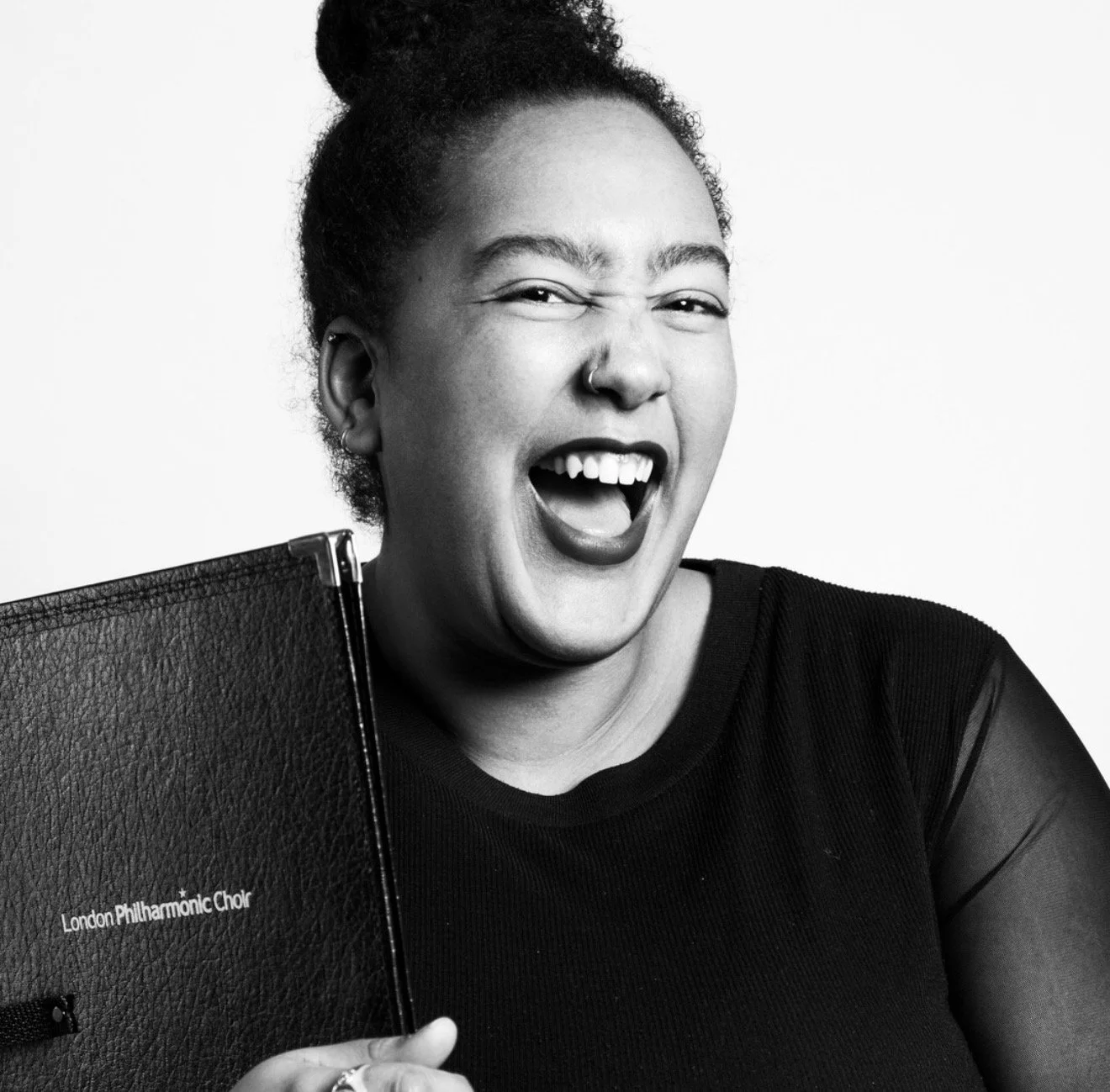 A woman with curly hair smiling and holding a booklet labeled 'London Philharmonic Choir'.