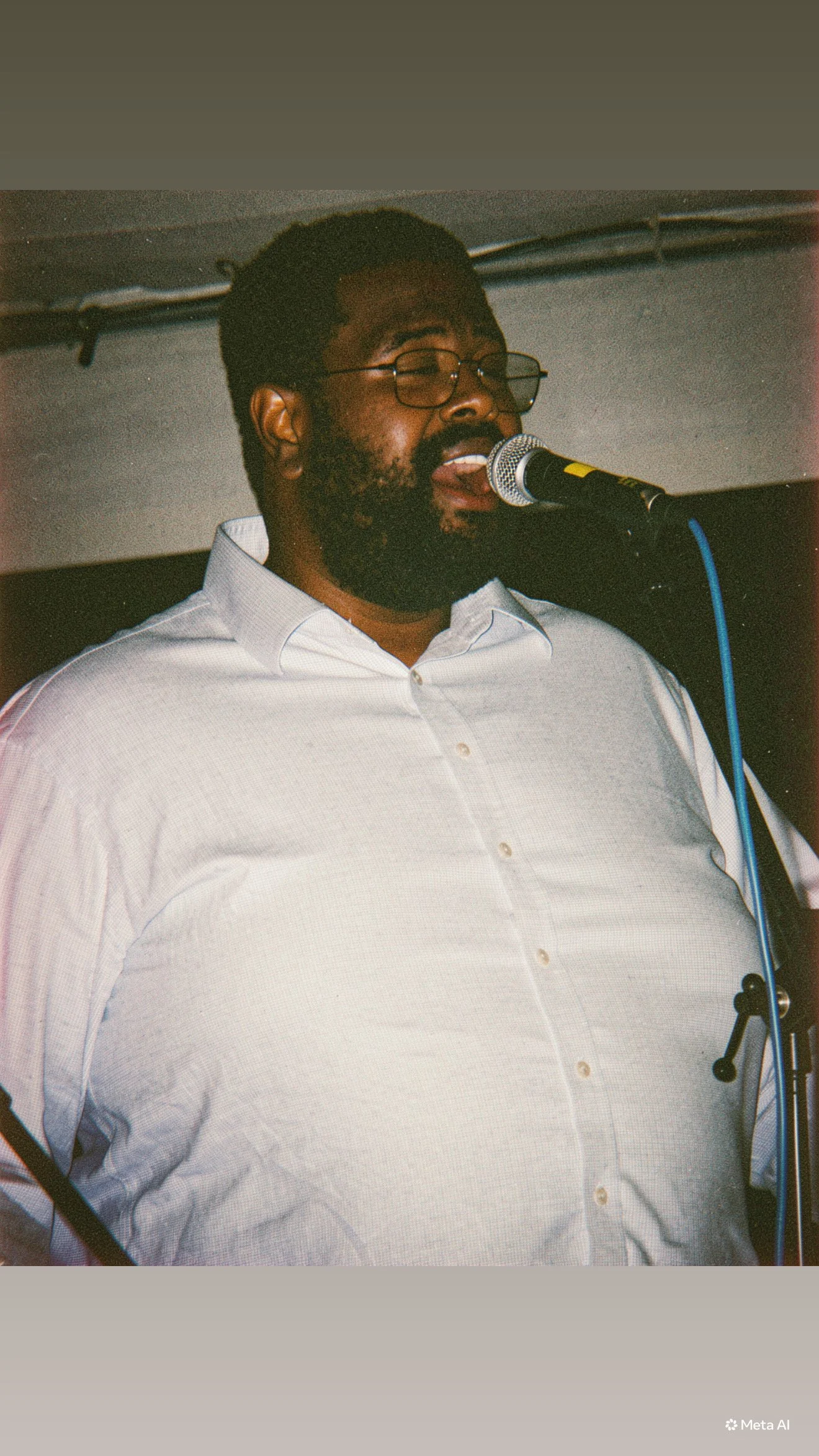 A man with glasses and a beard wearing a white button-up shirt singing or speaking into a microphone.
