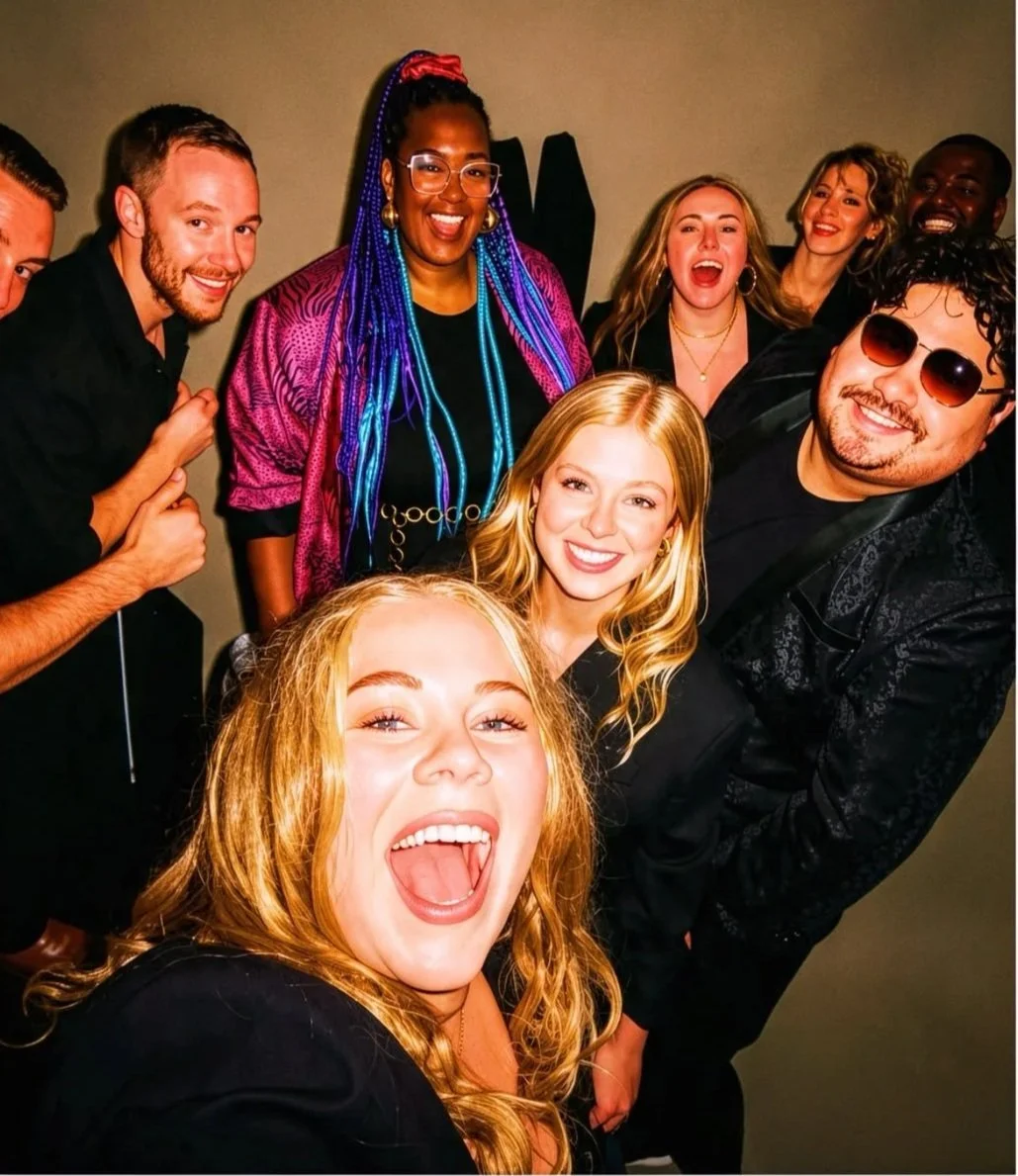 A group of young adults smiling and enjoying themselves at a social gathering or party, with some making excited gestures, against a neutral background.