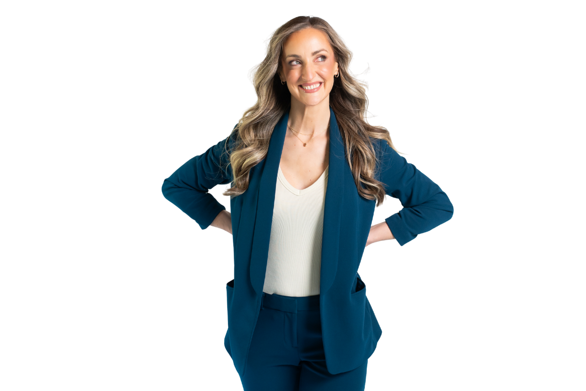 A woman with long wavy hair, wearing a teal blazer over a cream top, smiling confidently with her hands on her hips.