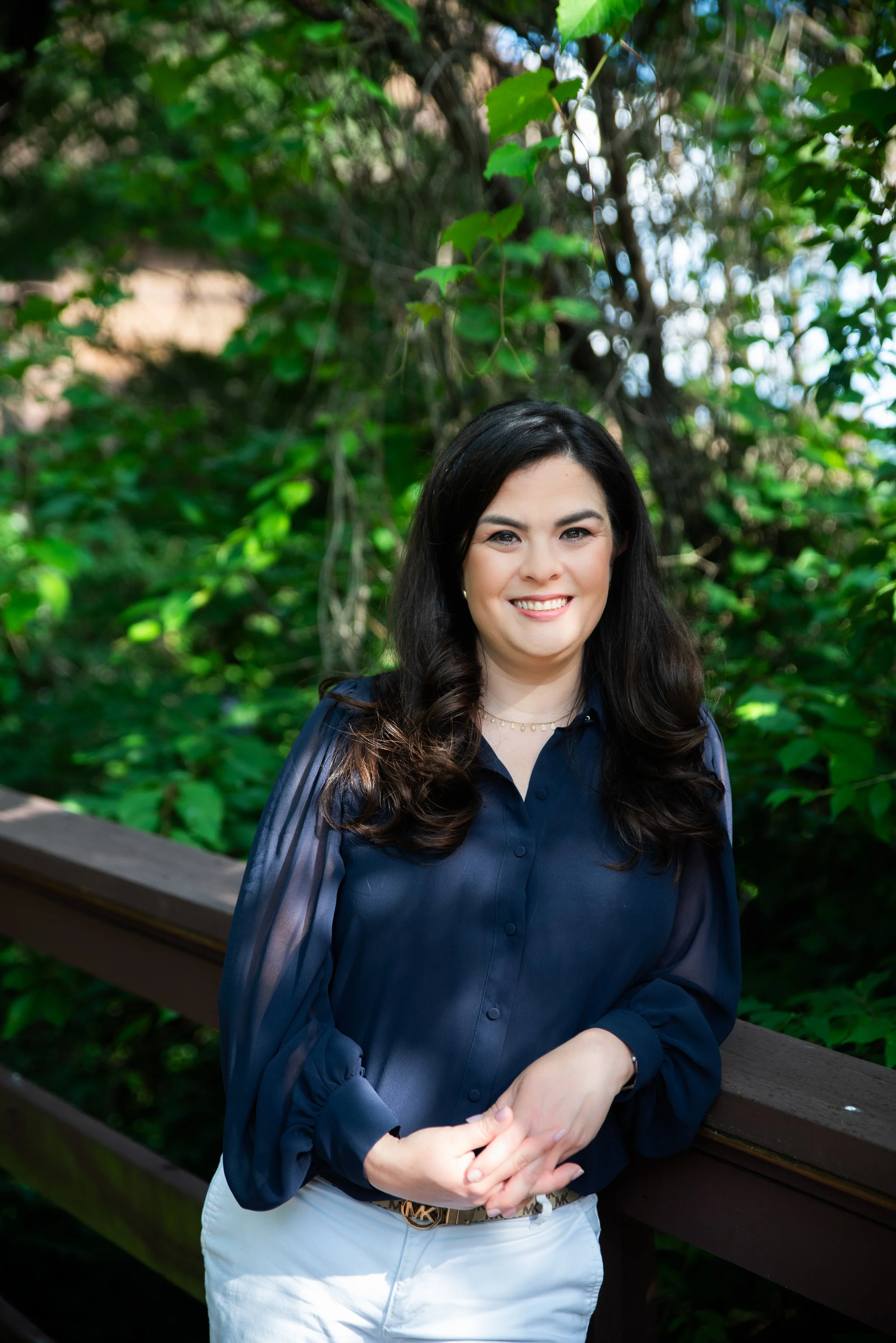Photo of Brittany Vera, LCSW, a trauma therapist who is a woman with long brown hair wearing a navy blue blouse, located outside on a bridge