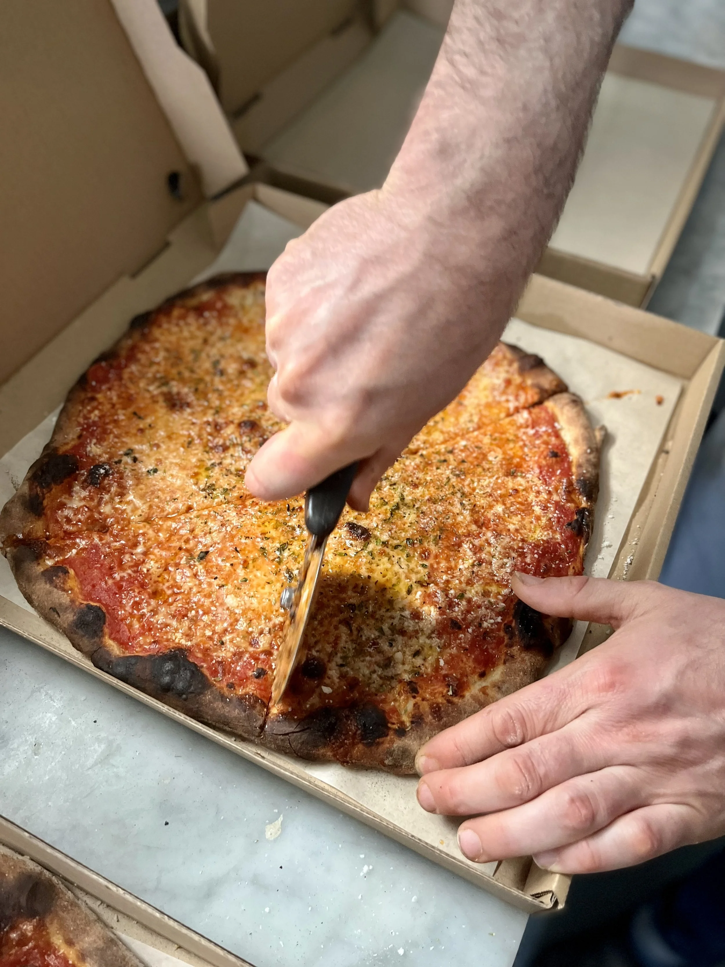 A person slicing a rectangular pizza with a knife in a pizza box.