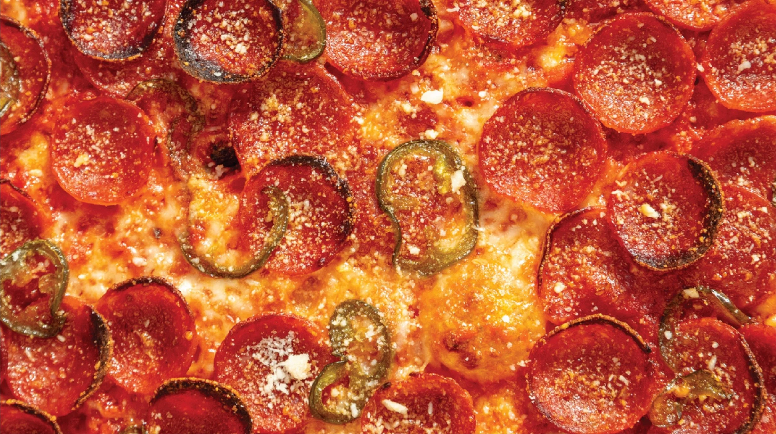 Close-up of a pepperoni and jalapeño pepper pizza with cheese and seasoning.