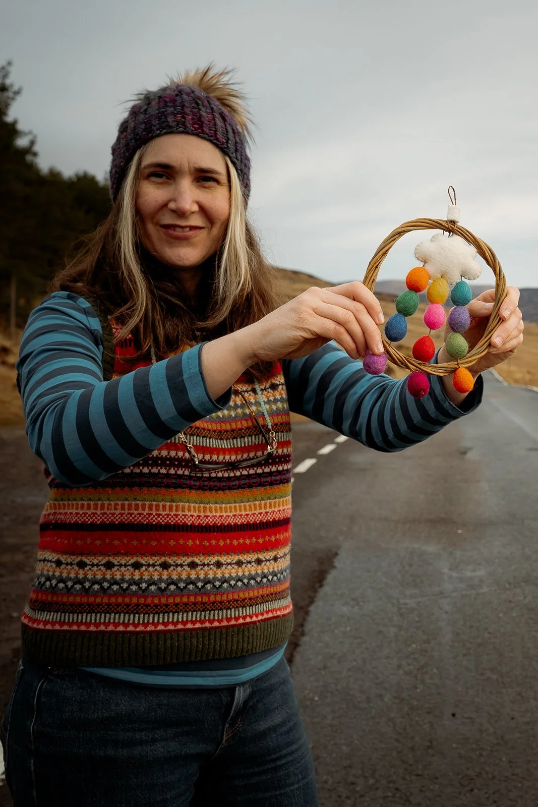 Feltmaker Tamzen holding a willow and wool dreamcatcher with rainbow baubles