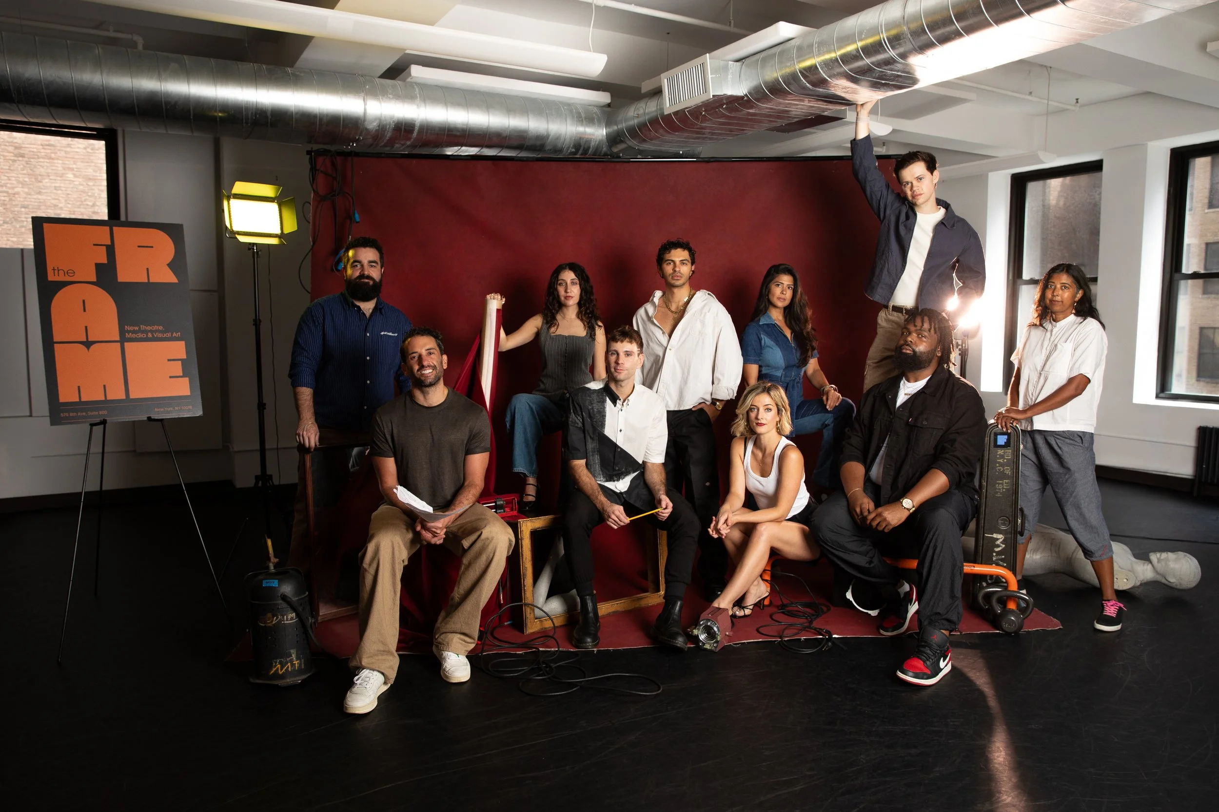 Group of diverse people posing in a photo studio with professional lighting, a red backdrop, and equipment, all looking at the camera.