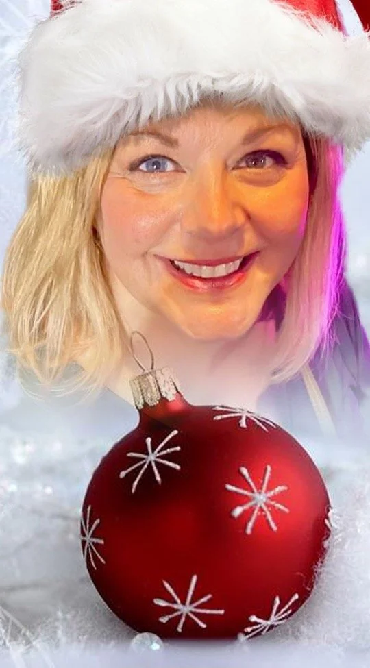 Jill from Jills wrap studio wearing a Santa hat smiling in front of a Christmas ornament on snow.