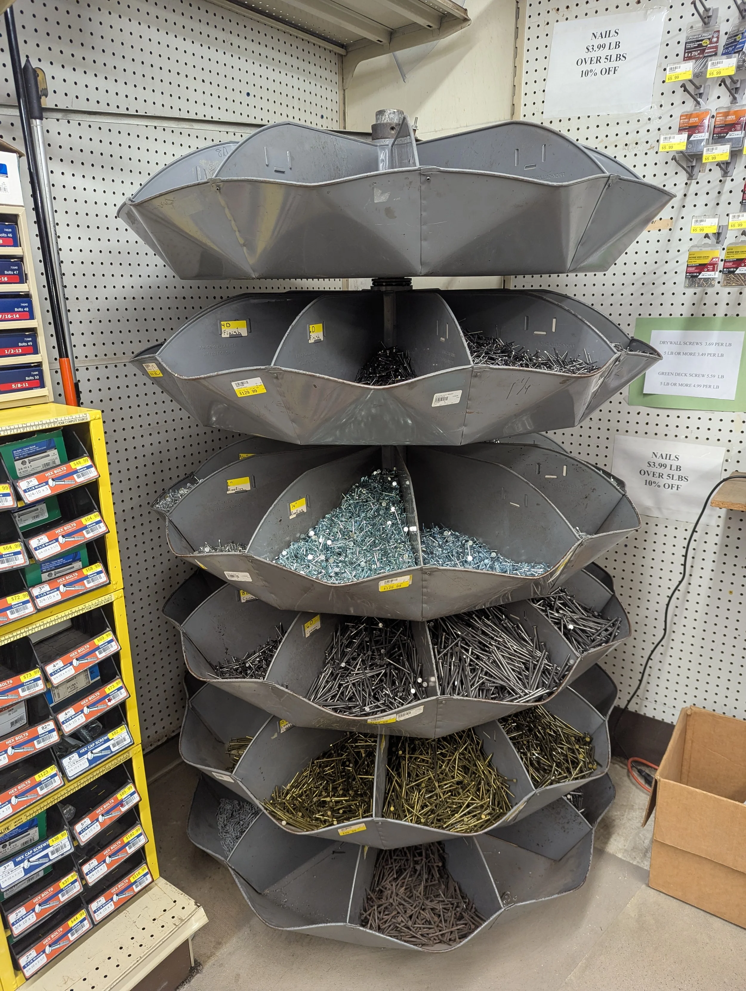 Metal buckets filled with different types of nails and screws arranged on a multi-tiered display in a hardware store.