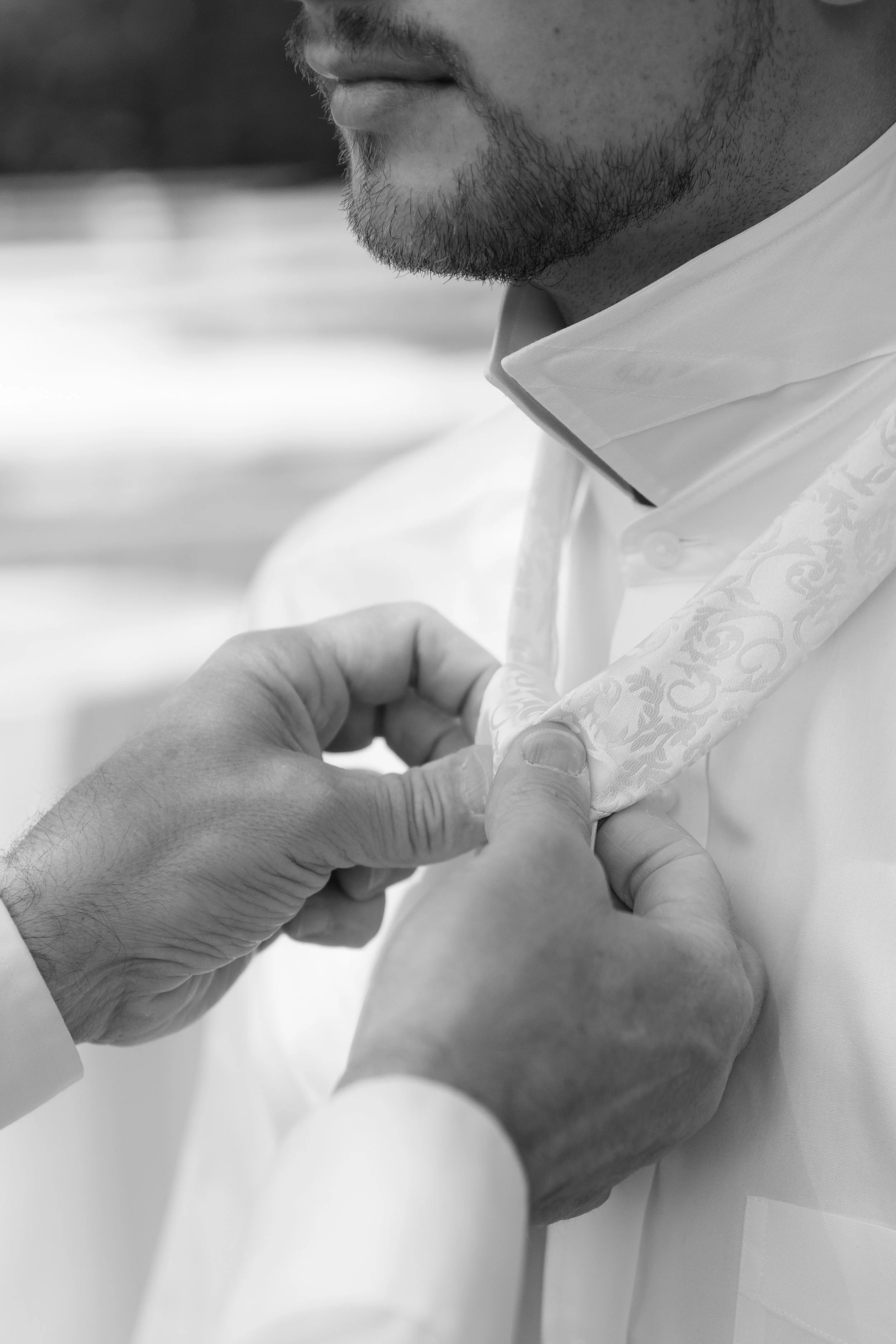 A person adjusting a white, patterned garment near their chest, with another person's hand helping.