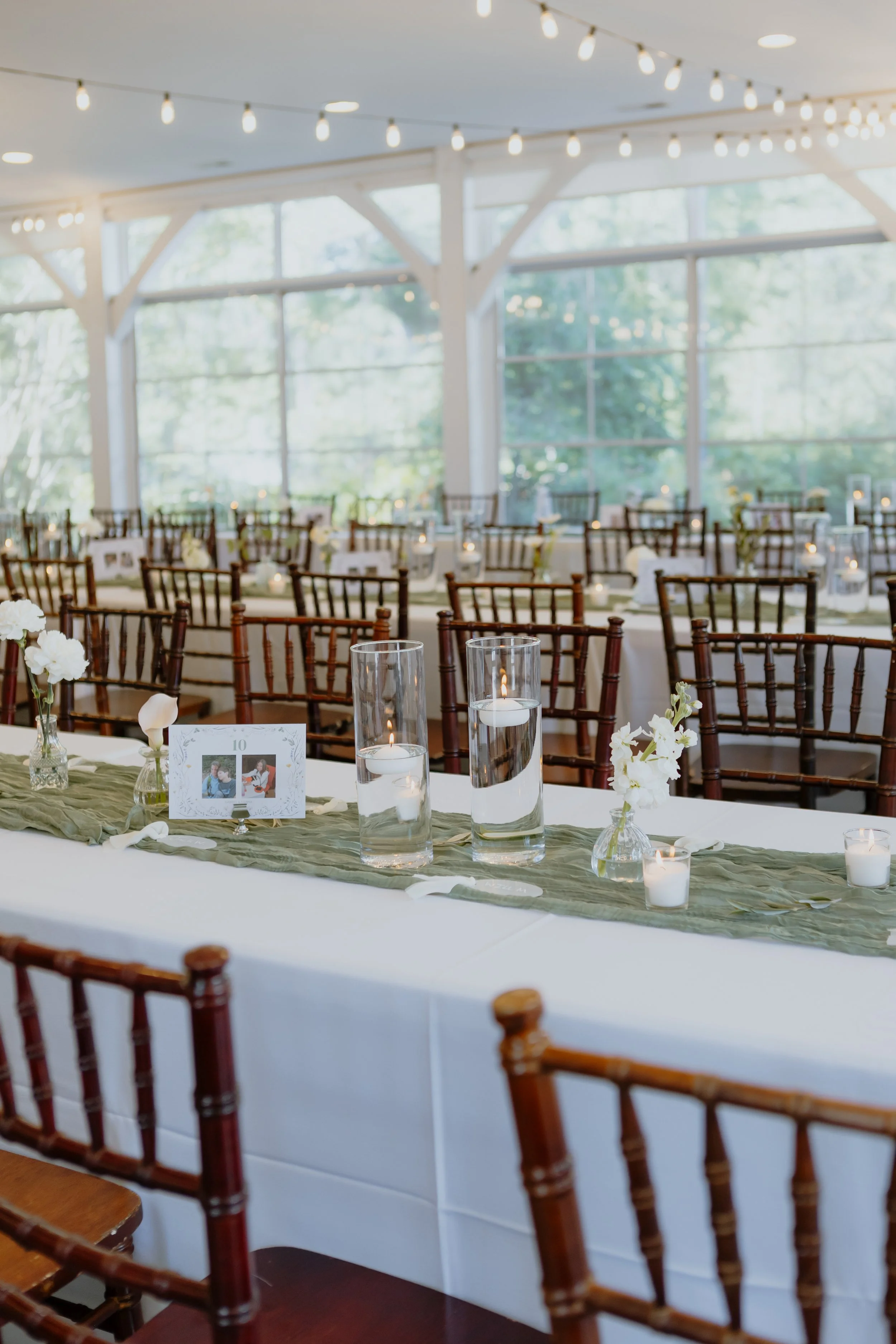 Event space decorated for a wedding reception with string lights and round tables with white tablecloths, floral centerpieces, and candles.