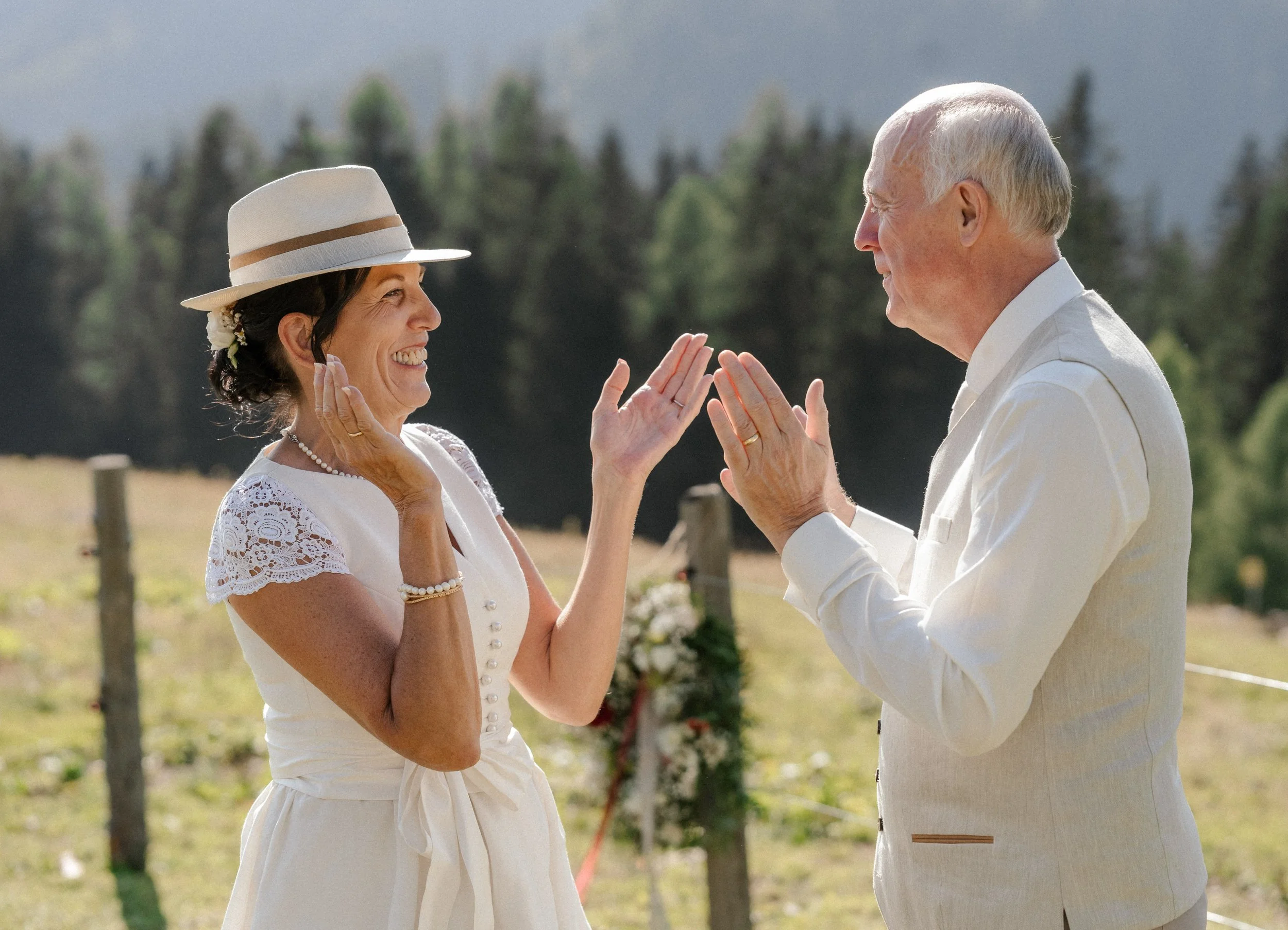 Ein Mann und eine Frau, die sich bei einer Hochzeit im Freien die Hand halten und lächeln.