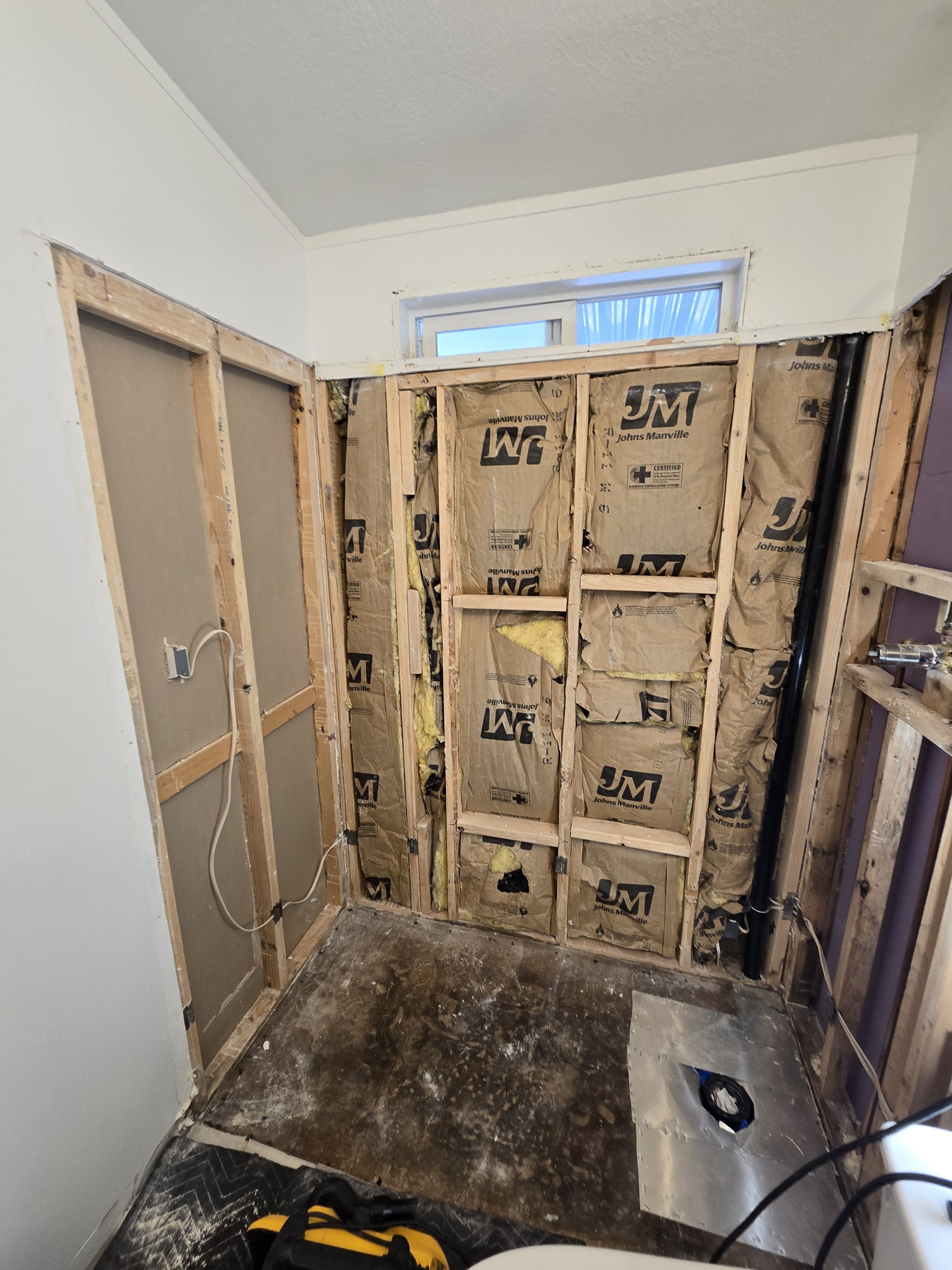 Partially demolished wall with exposed insulation and framing inside a room undergoing renovation, with construction tools on the floor.