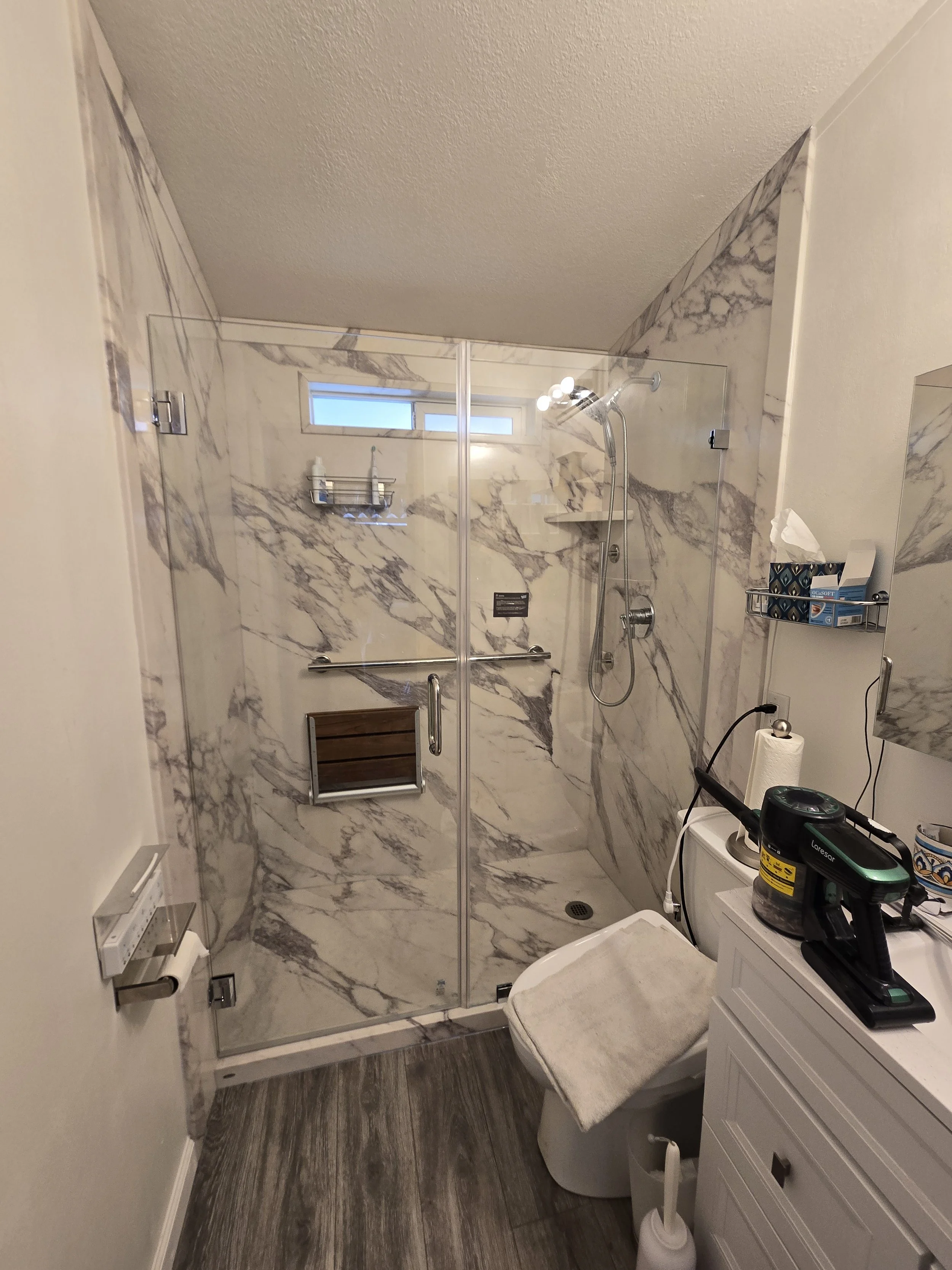 A modern bathroom with a modern shower enclosure, a small window, and a white vanity. New accessories, a toilet, and various toiletries on a shelf inside the shower.
