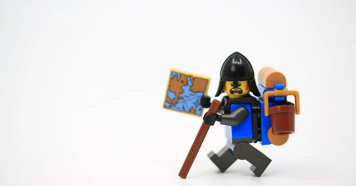 Male lego explorer holding a map and a walking stick while carrying a backpack