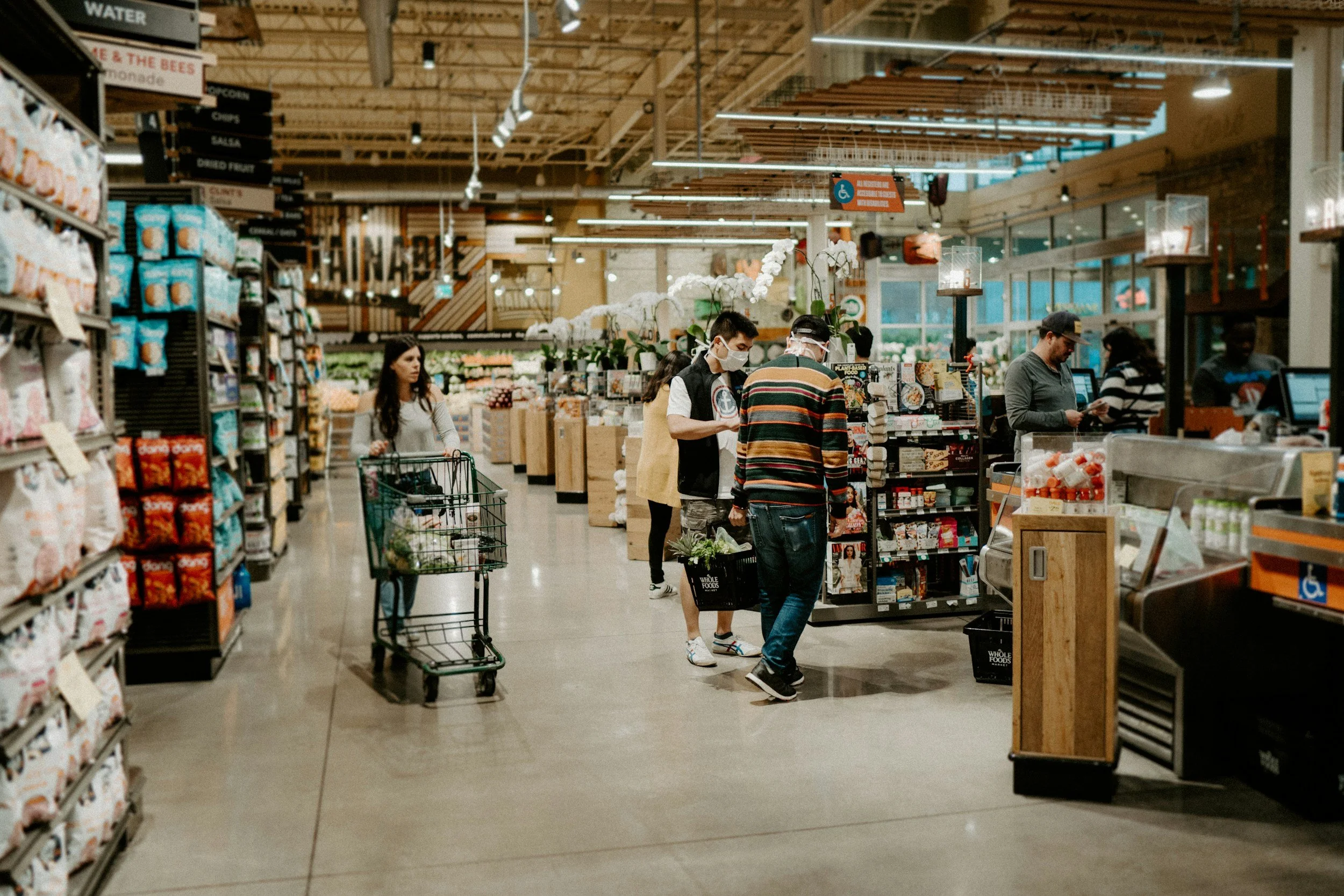 People shopping in a supermarket aisle with shelves stocked with food products.