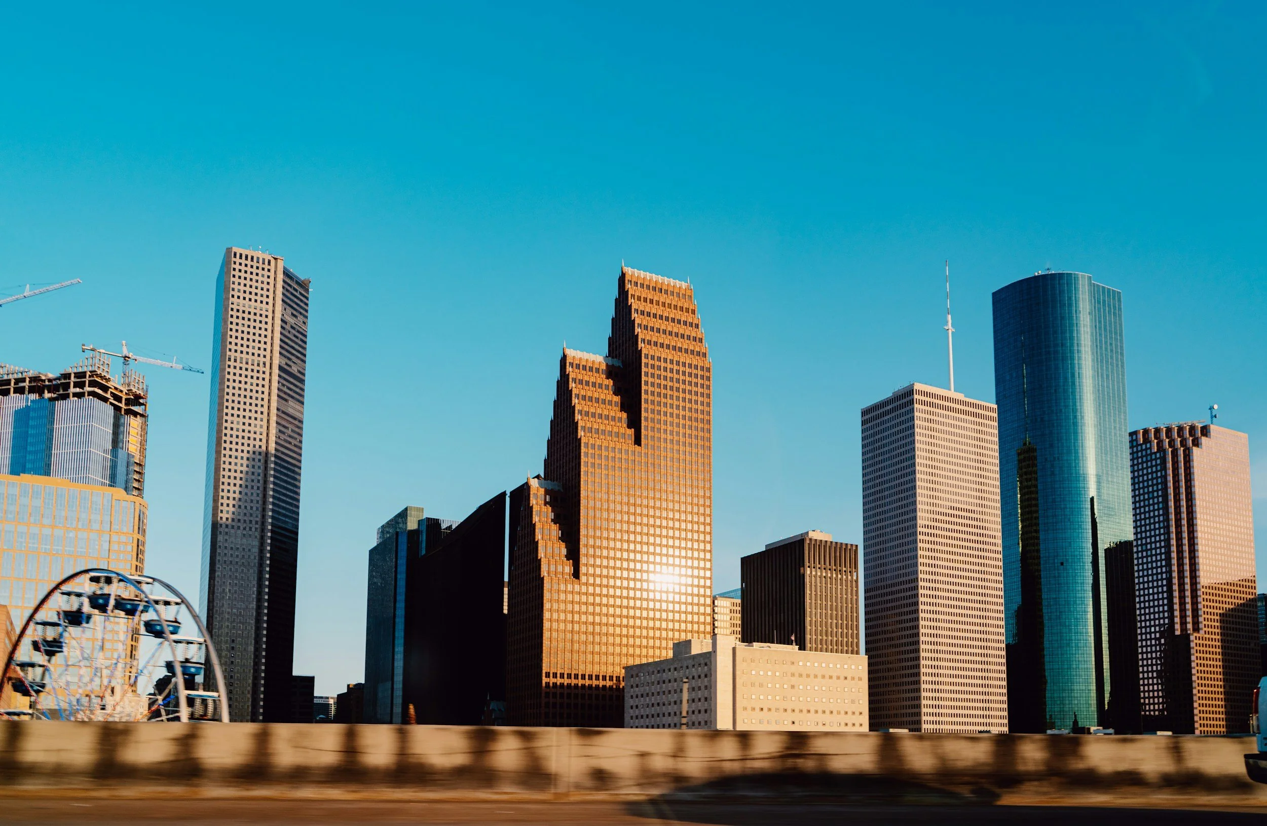 Tall skyscrapers in a city skyline during daytime with a clear blue sky, and a Ferris wheel visible on the left side of the image.