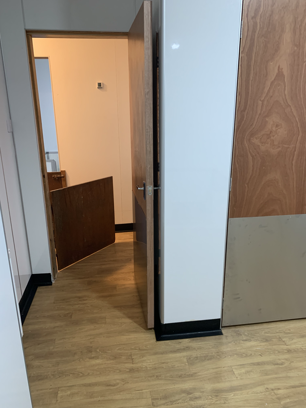 Empty room with wooden flooring, partially open wooden door, and a view into another room or hallway