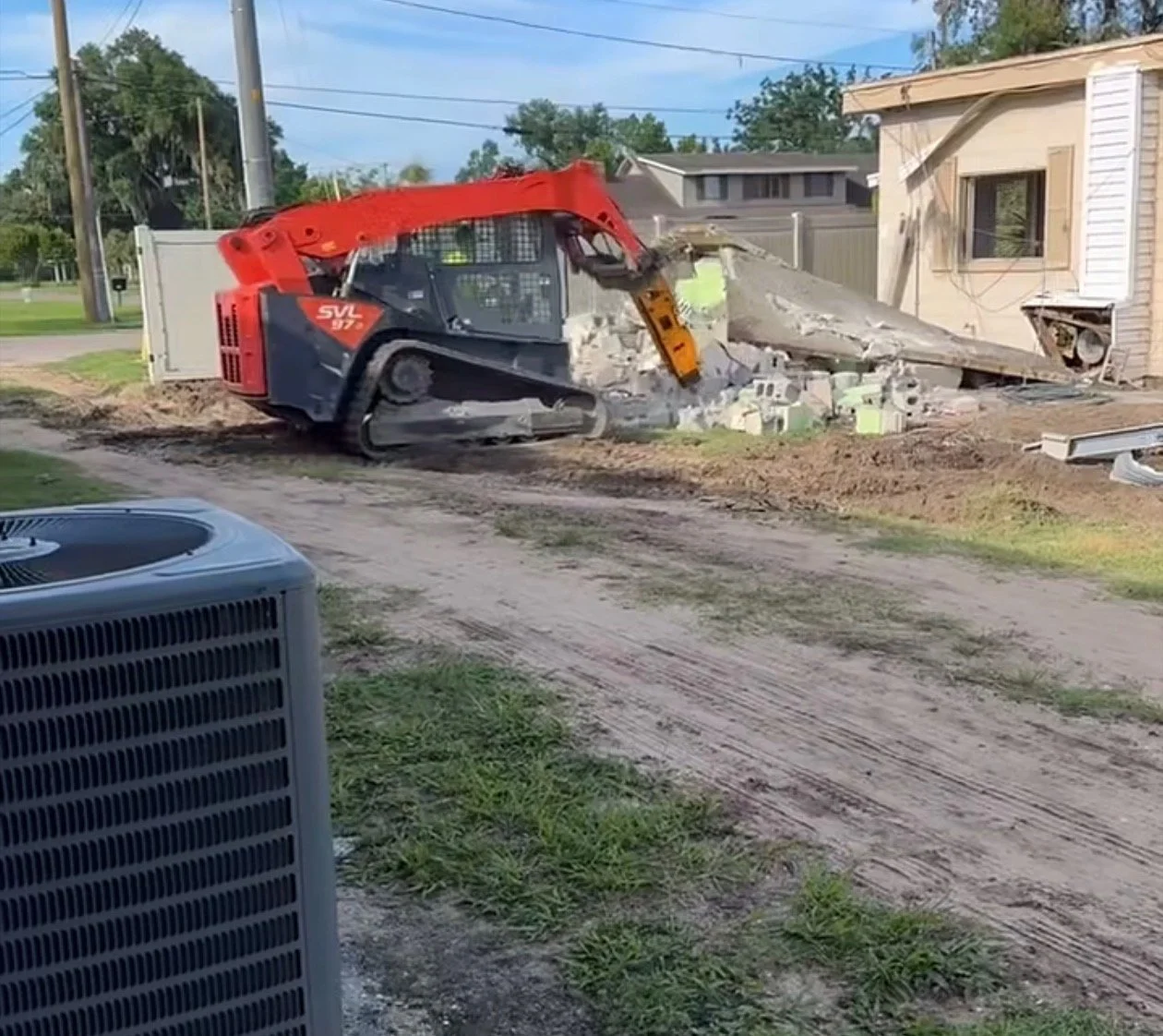 A skid-steer loader demolishing a small house with debris scattered around.