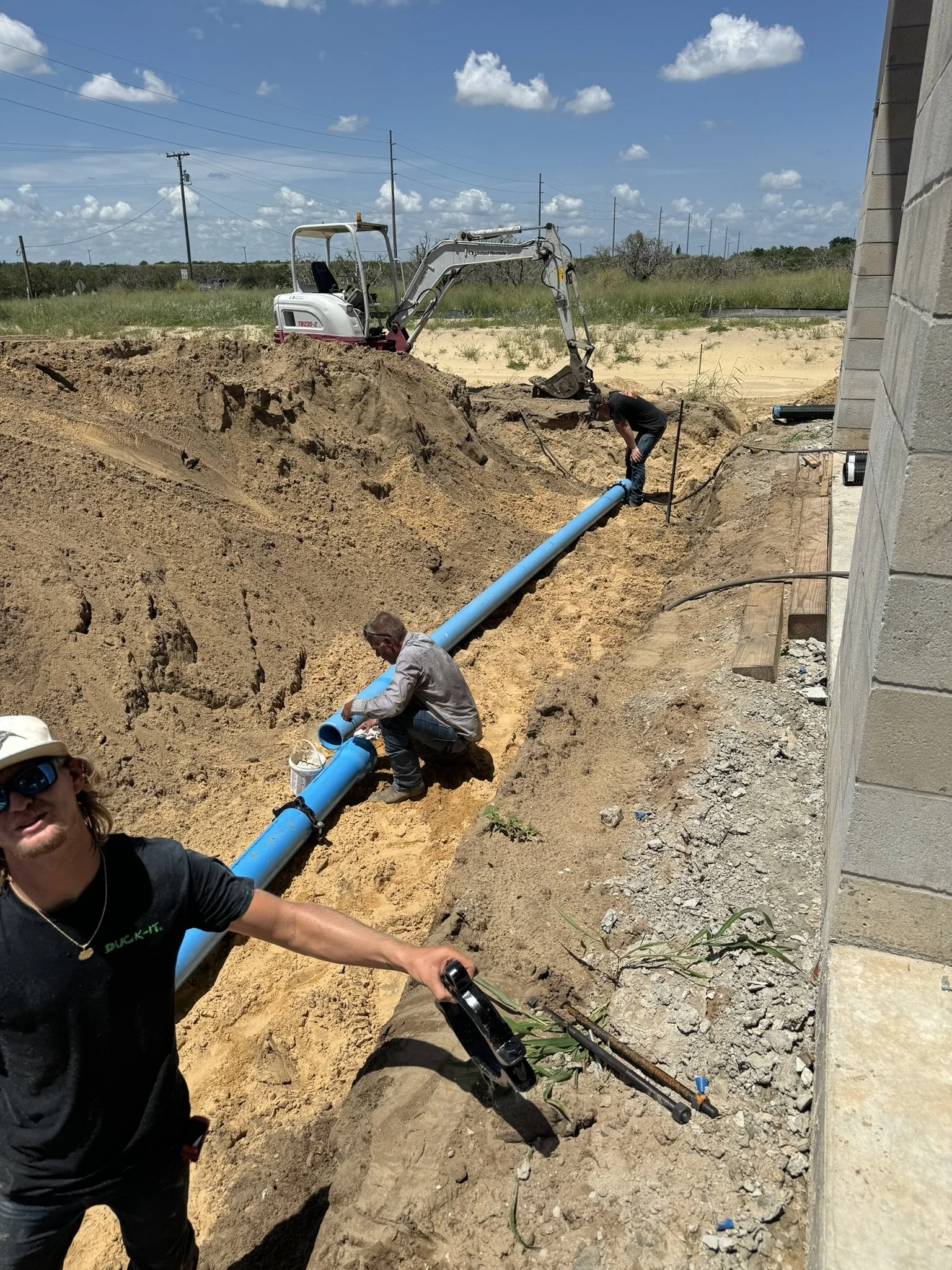 People working on installing a blue pipe underground near a house with a construction area and excavated soil.