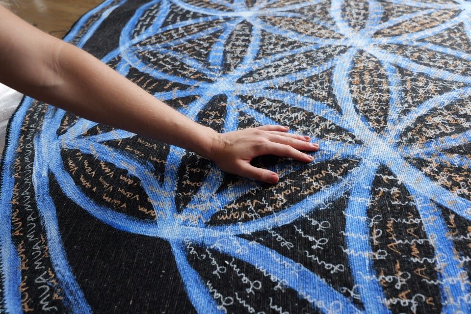 Child's hand reaching on a circular, patterned rug with blue, black, and brown colors.