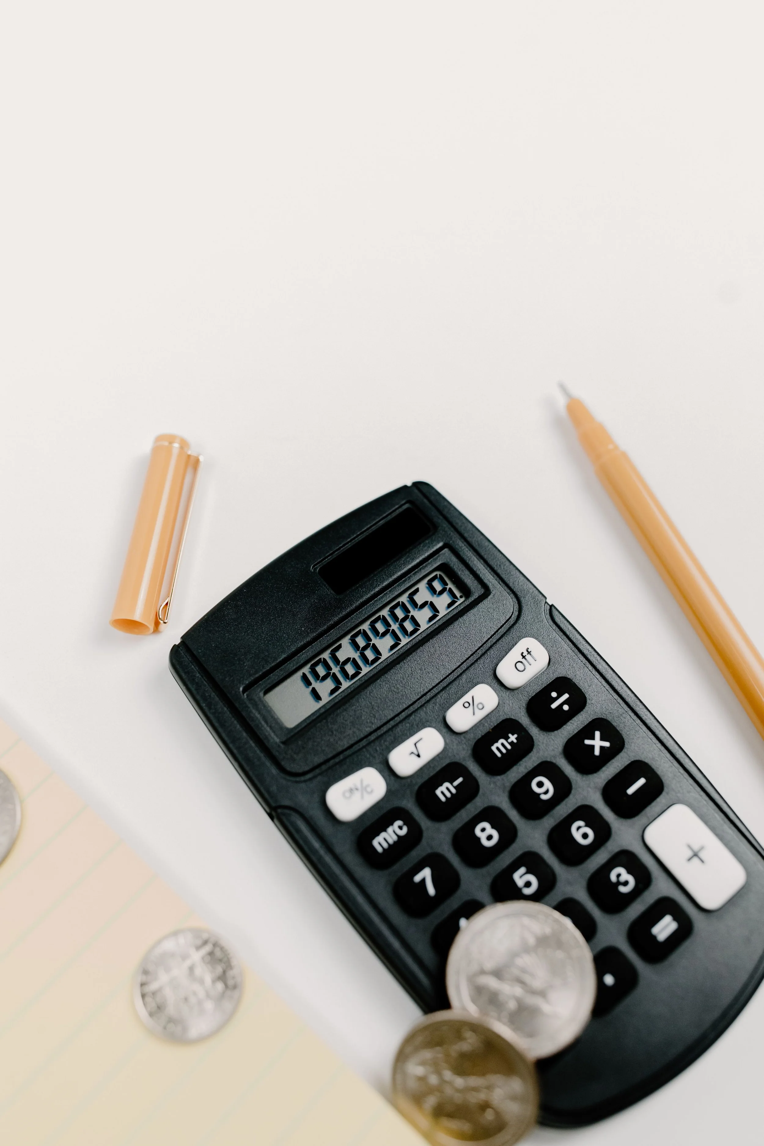 A calculator displaying the number 1,968,909,159, along with coins and a pen on a white surface.