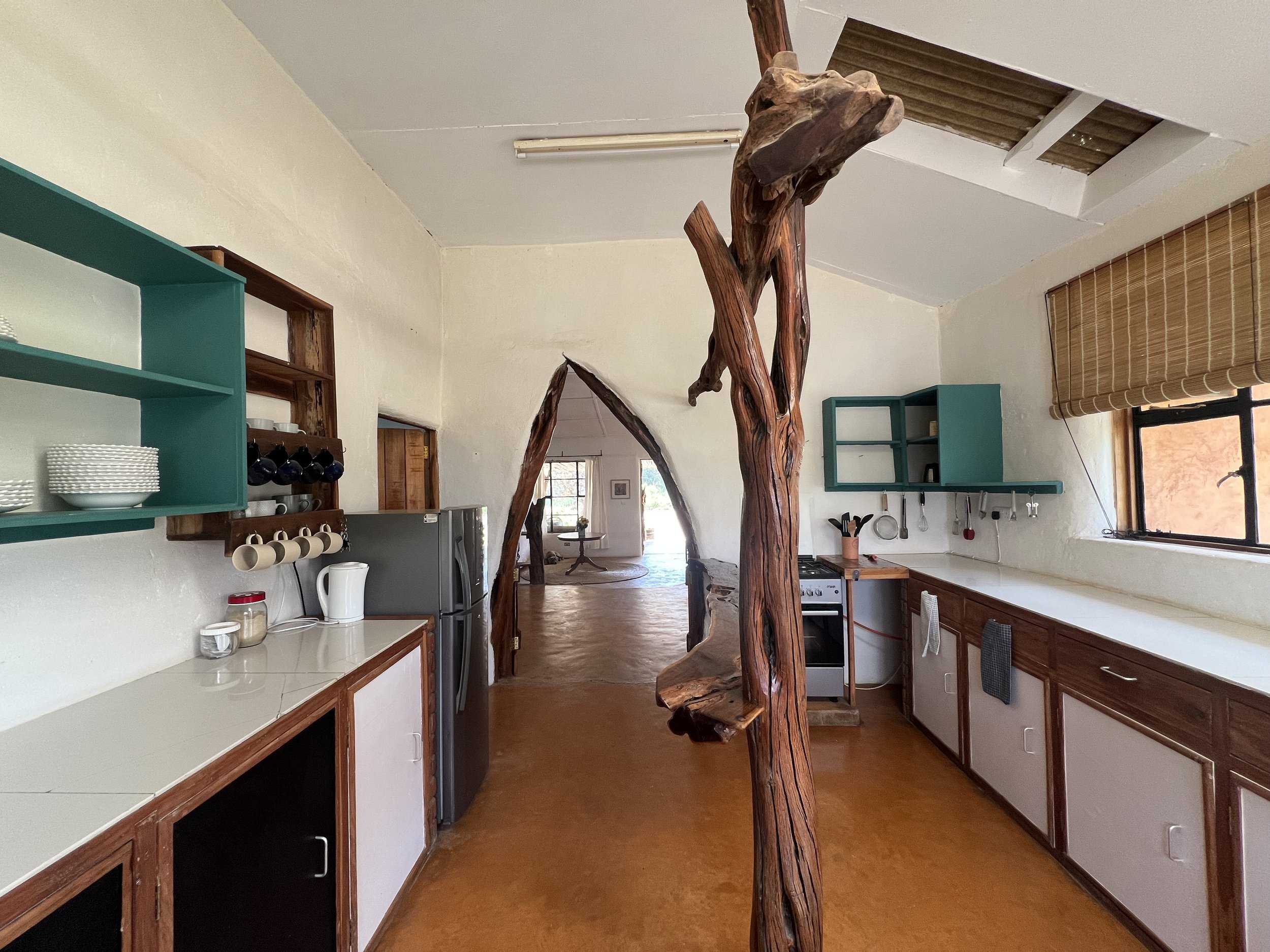 Rustic kitchen with open shelving, teal cabinets, and a large wooden sculpture of a tree branch in the center.
