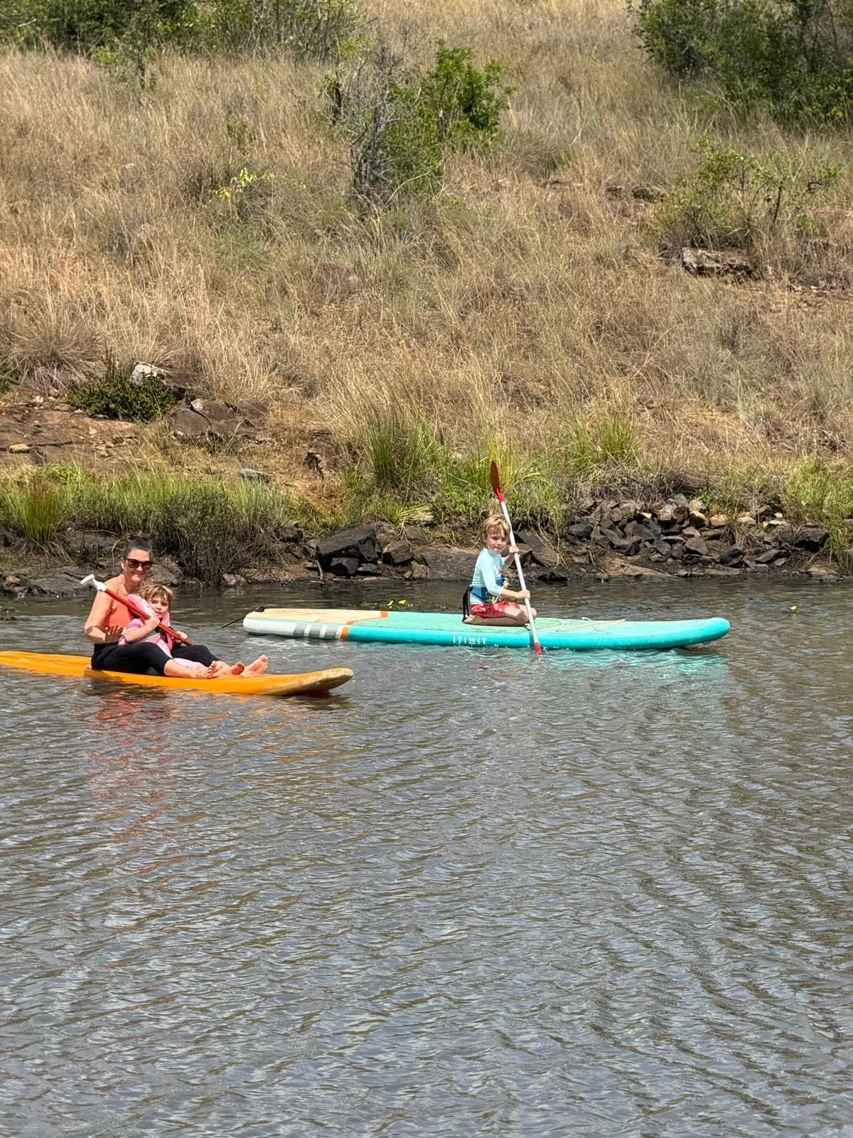 Mother and two children enjoying a day on the water; one child kayaking, while the mother and other child are paddling on a paddleboard.