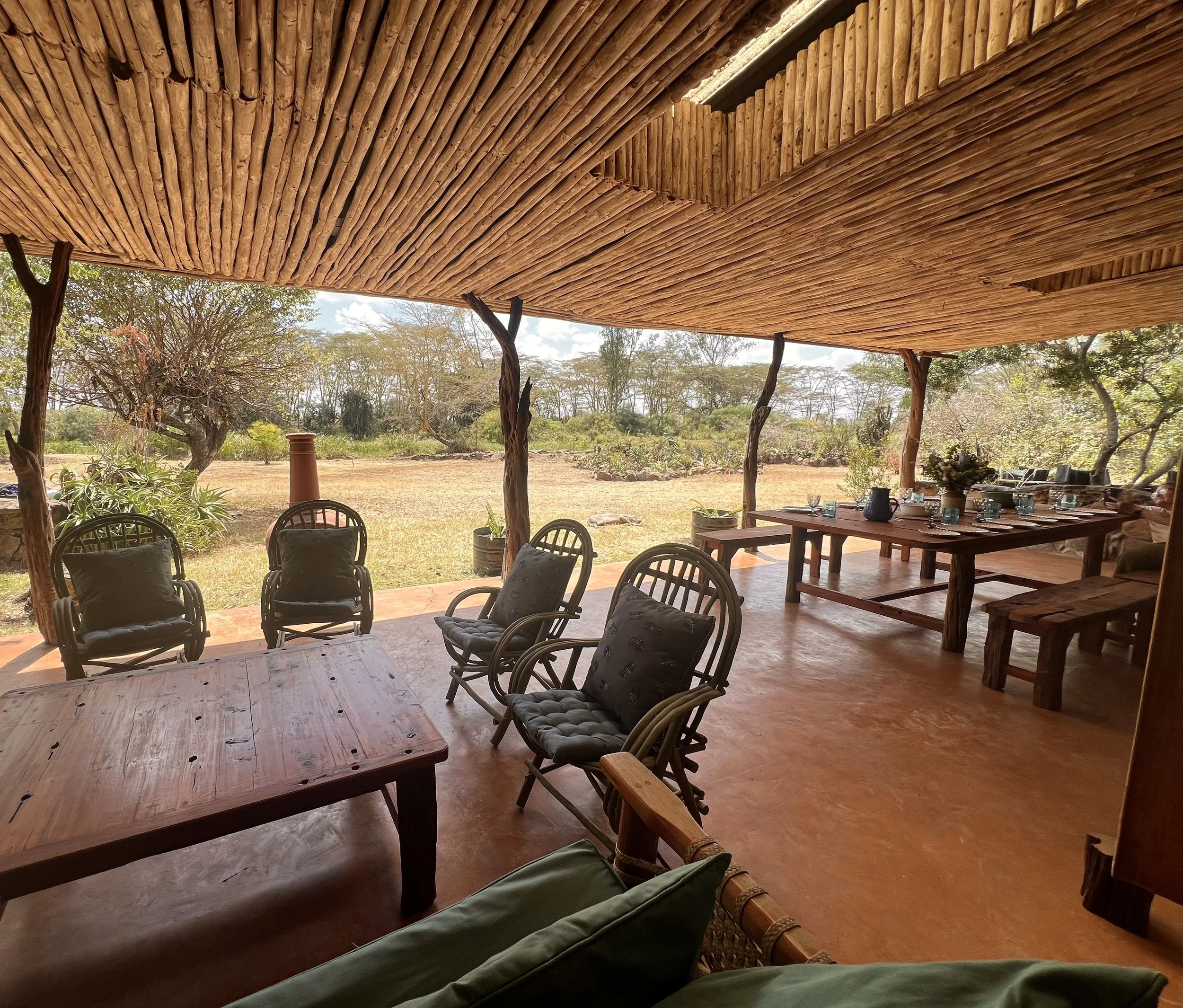 Outdoor covered dining area with wooden furniture, surrounded by trees and natural landscape.