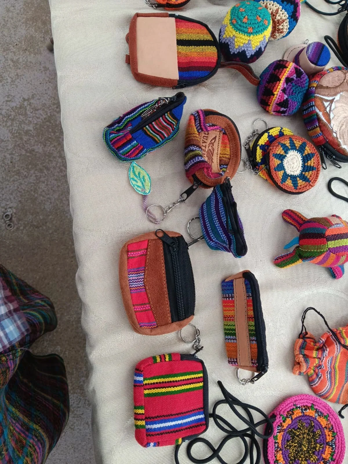 A table displaying handmade colorful woven accessories including small pouches, keychains, and decorative items, many featuring traditional patterns.
