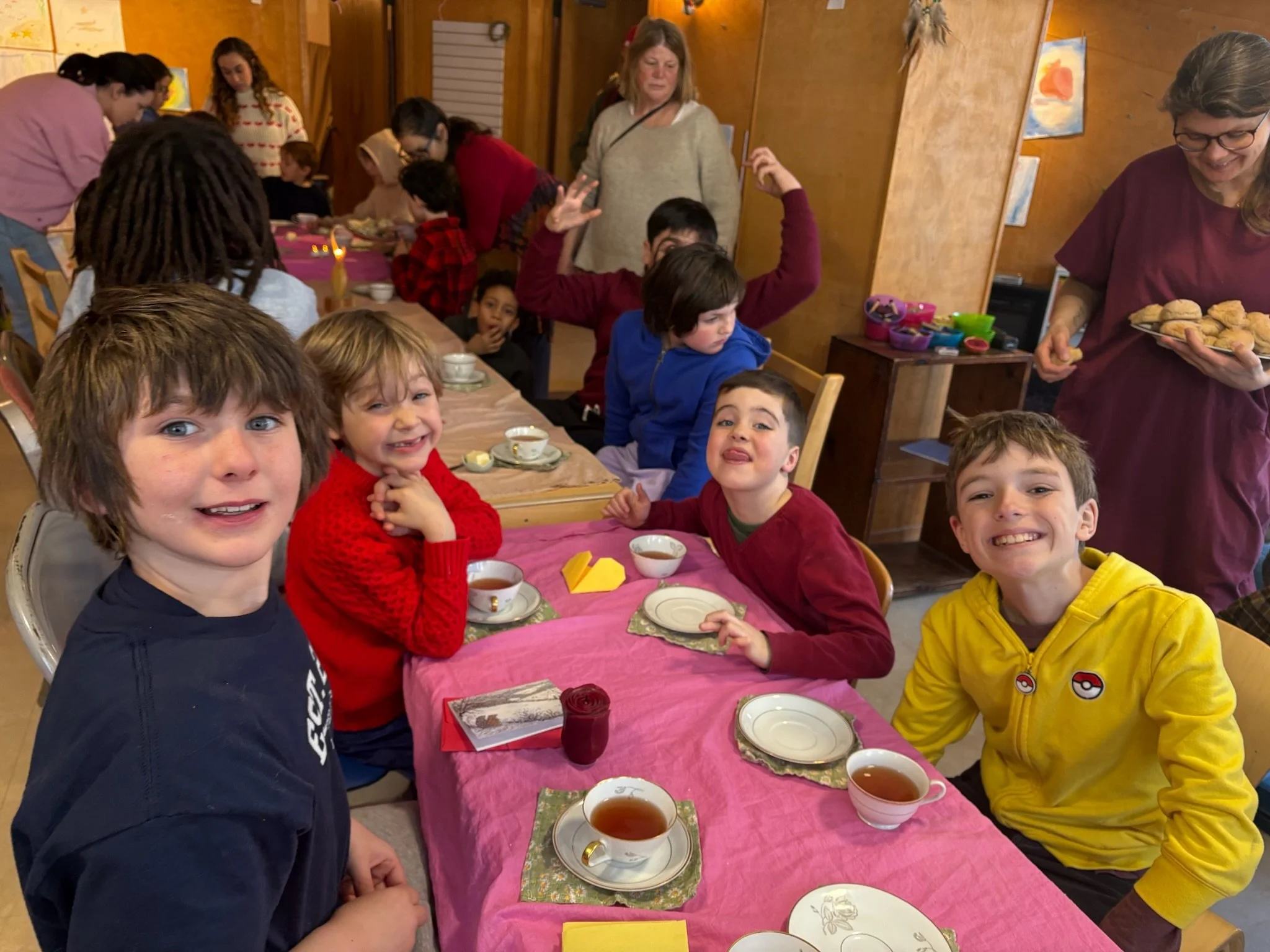A group of young male students smile at the camera while sitting down at a long table for cups of tea and snacks.