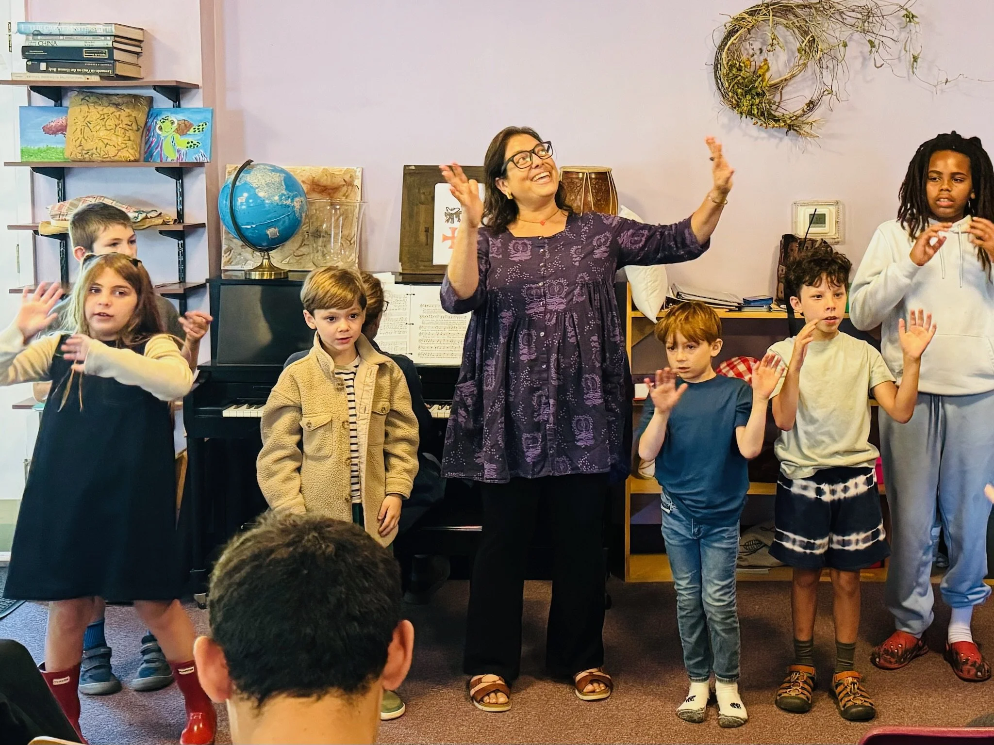 A group of young students at Otto Specht School are singing in a line with their teacher who is conducting them with her hands in the air.
