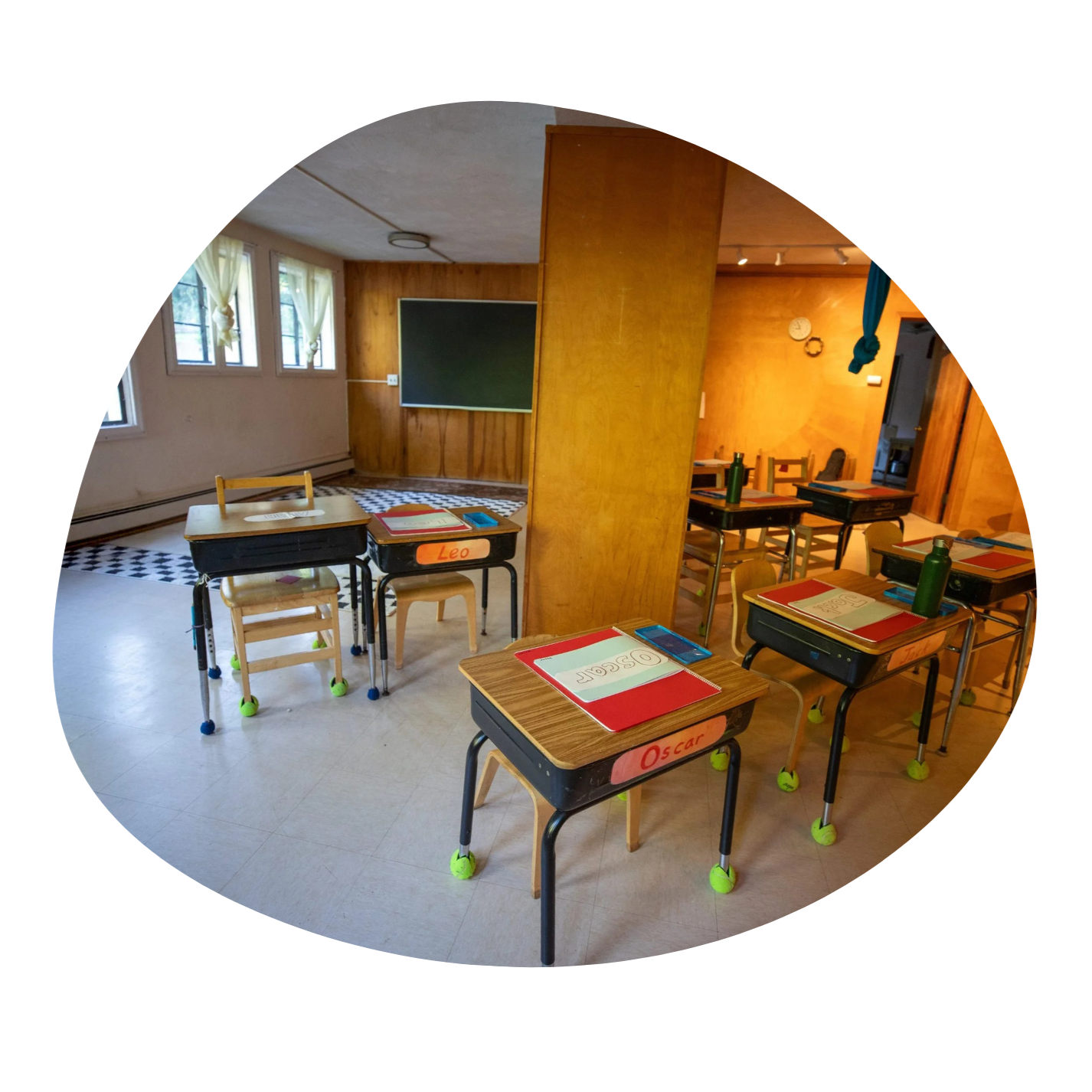 A classroom at Otto Specht School. The walls are a warm brown wood, and the desks have students names on the front on watercolor painted pieces of paper. The feet of the chairs and desks have tennis balls on them to prevent scratching the floor.