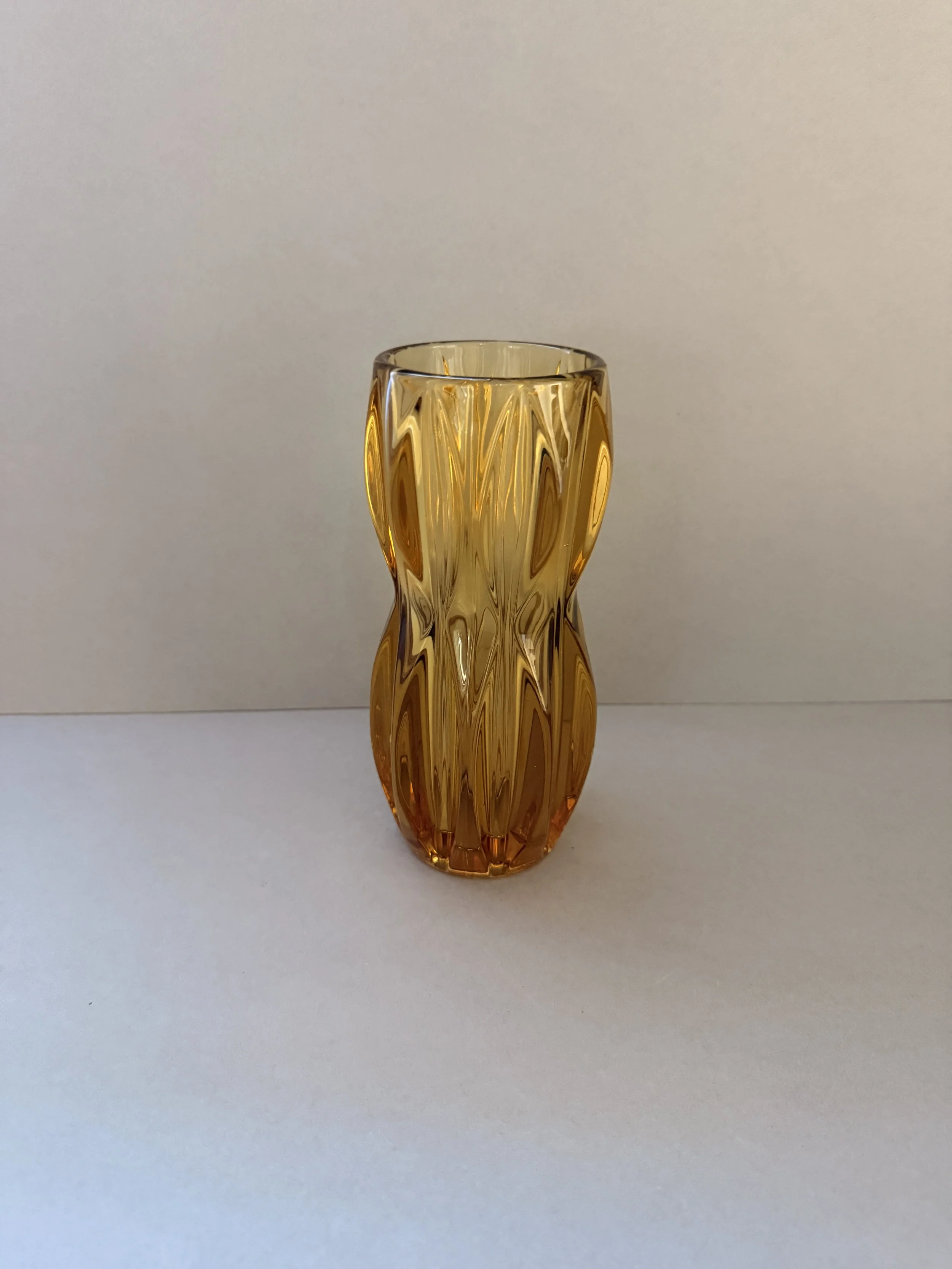 Amber-colored decorative glass vase with a geometric pattern, placed on a white surface against a plain white background.