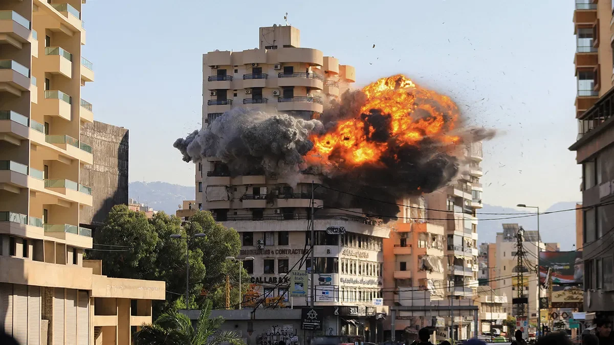 A large explosion and fire on a multi-story building between other high-rise buildings in an urban area.