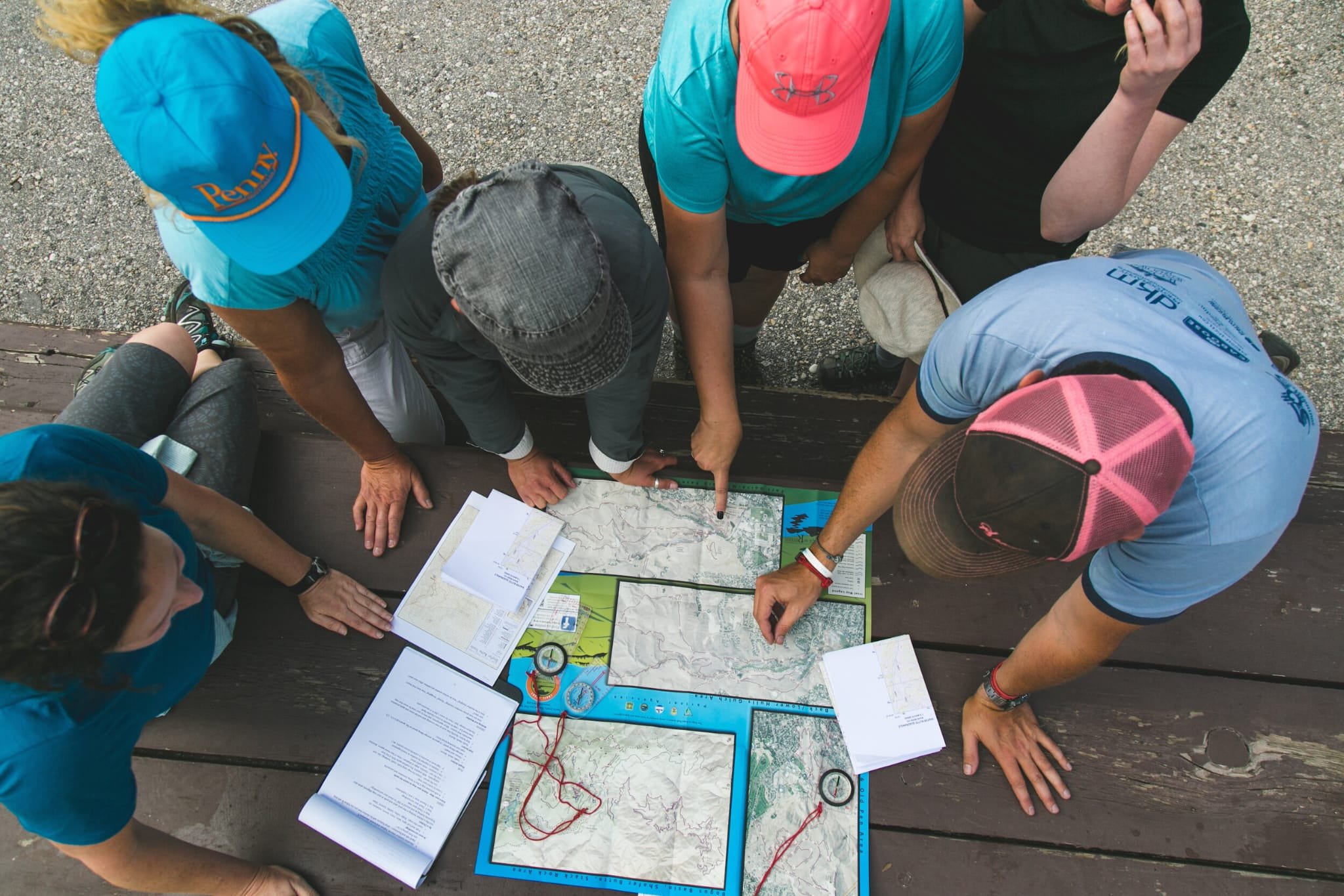 Een groep mensen die kaarten, papieren en navigatiehulpmiddelen bekijken, gekleed in outdoor-kleding en hoeden, mogelijk op een route of wandeling.