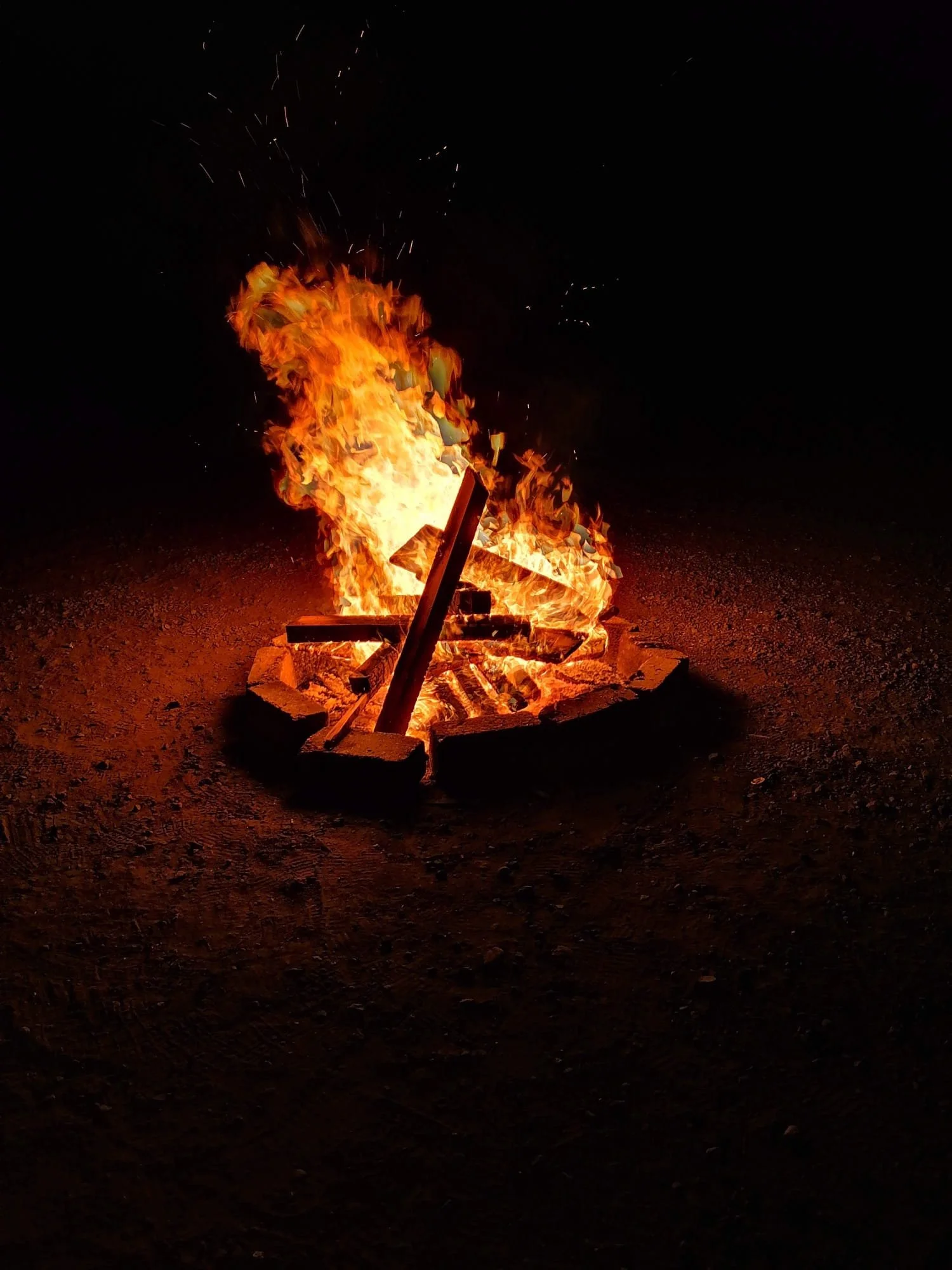 Een kampvuur met vlammen en brandende houten planken op een donkerdere achtergrond.