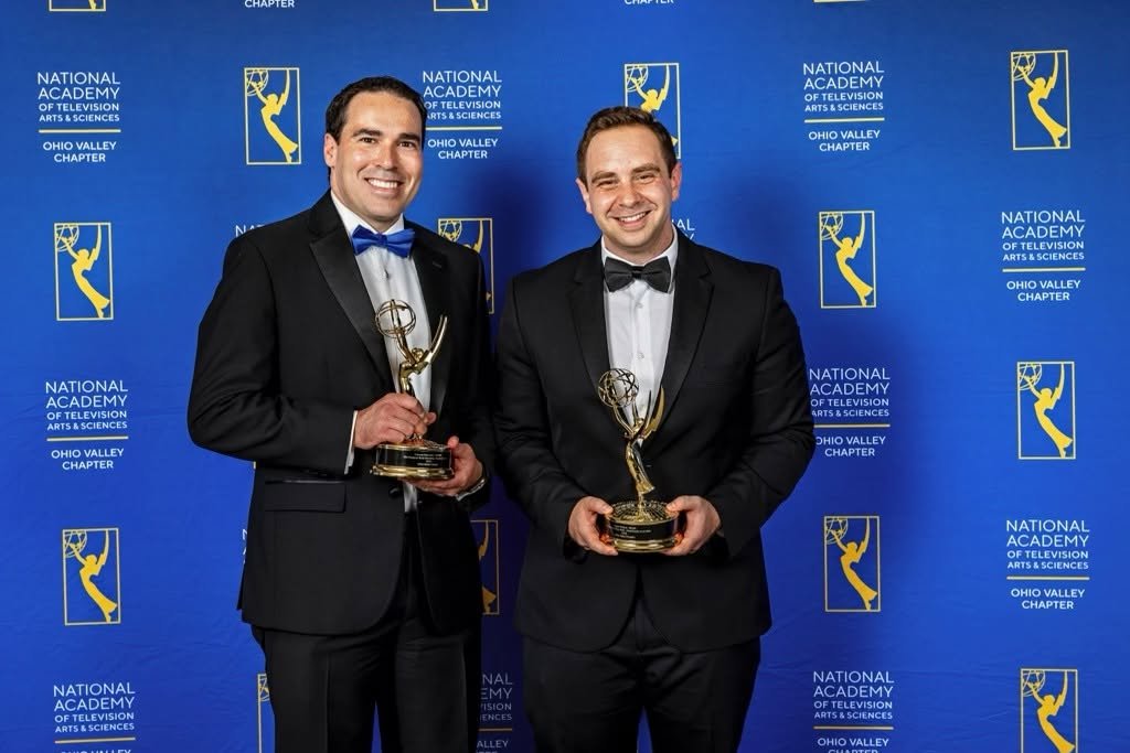 Two men in tuxedos holding Emmy awards, standing in front of a blue backdrop with the logo of the National Academy of Television Arts & Sciences Ohio Valley Chapter.