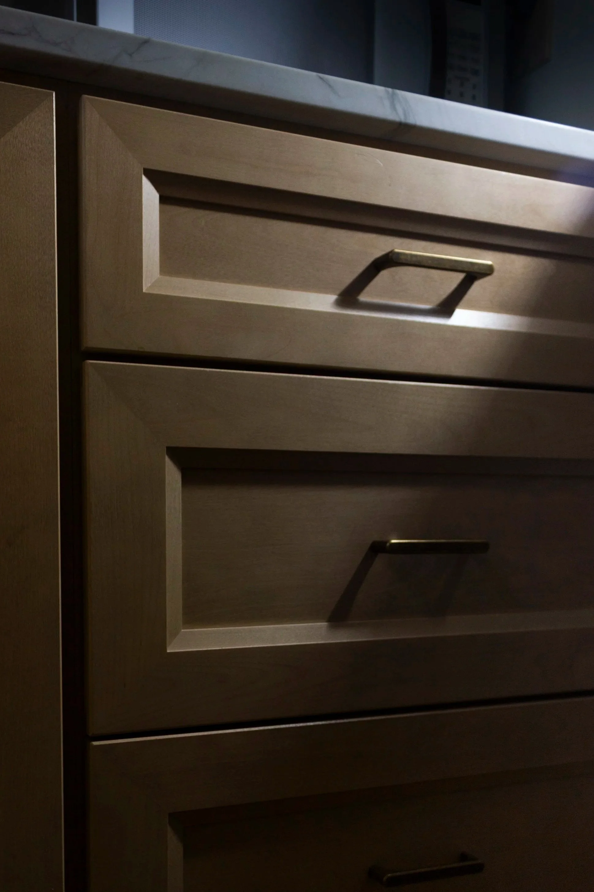 Moody photo of cabinets with brass handles and quartzite counter top.
