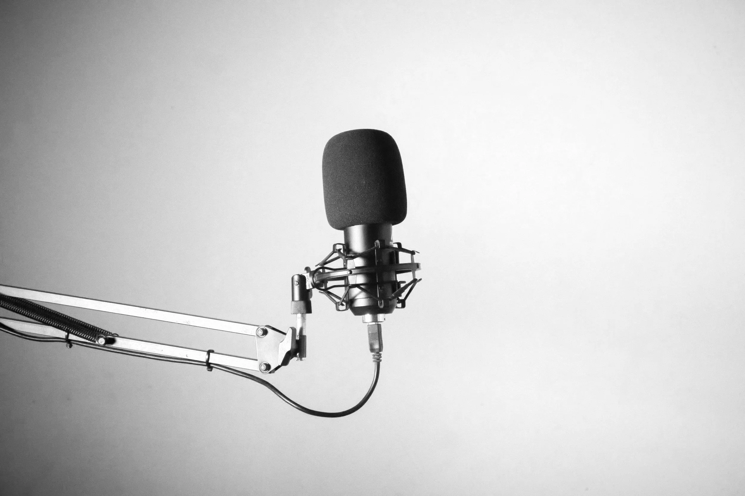A black microphone suspended from a stand with a long arm, against a plain light background.