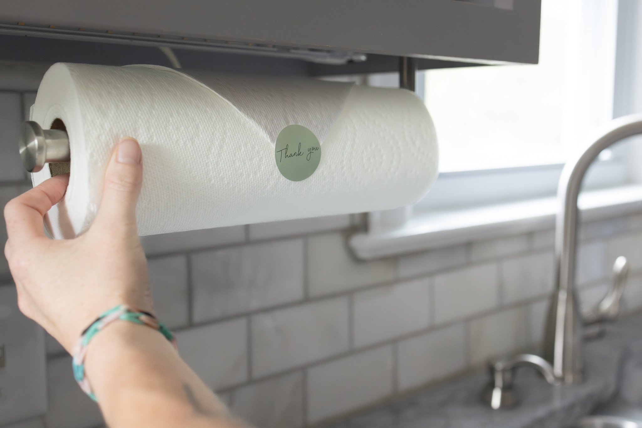 Hand removing a roll of paper towels from a metallic paper towel holder under a cabinet.
